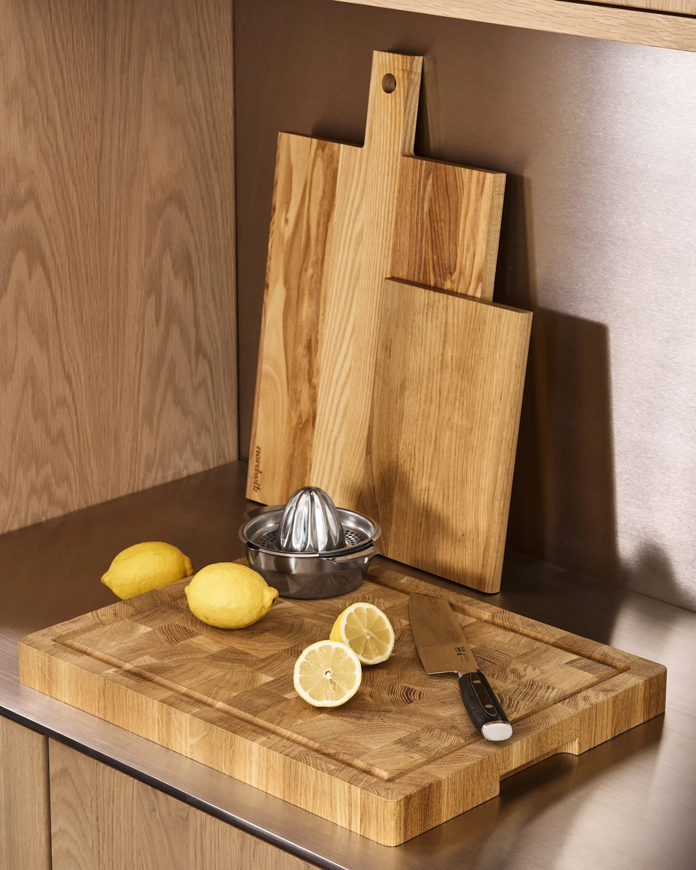 Trois planches à découper en bois, un presse-agrumes en acier inoxydable, des citrons entiers et coupés sur un comptoir de cuisine.