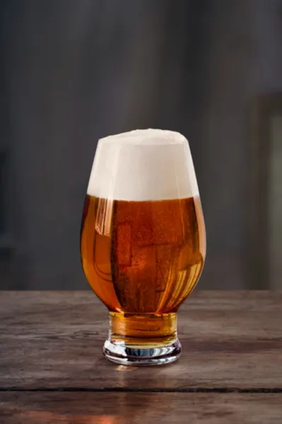 Verre tulipe de bière ambrée avec une épaisse mousse blanche sur une table en bois rustique.