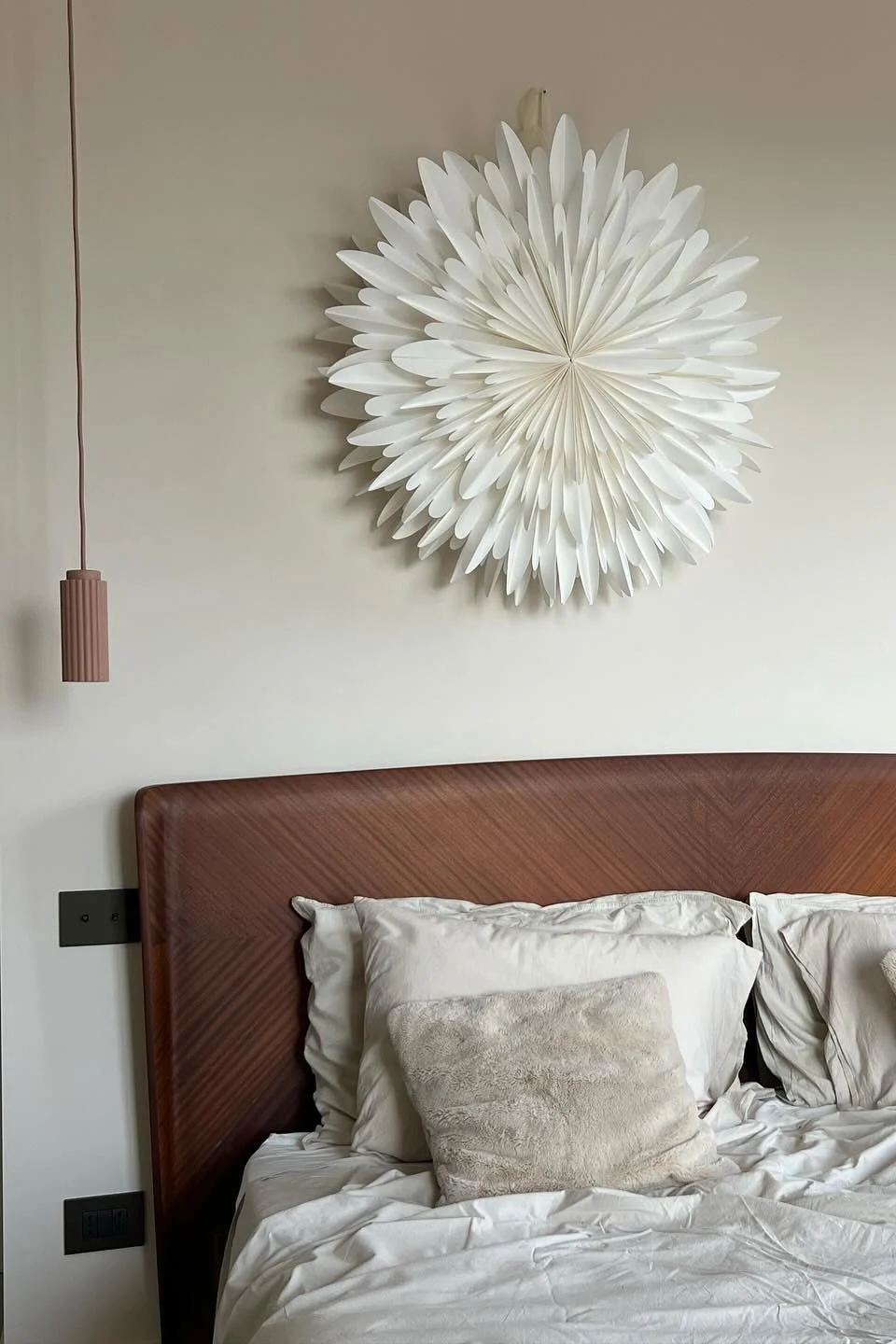 Chambre avec un lit, une tête de lit en bois, de la literie blanche, des oreillers moelleux, deux suspensions et une décoration murale étoile en papier blanc.