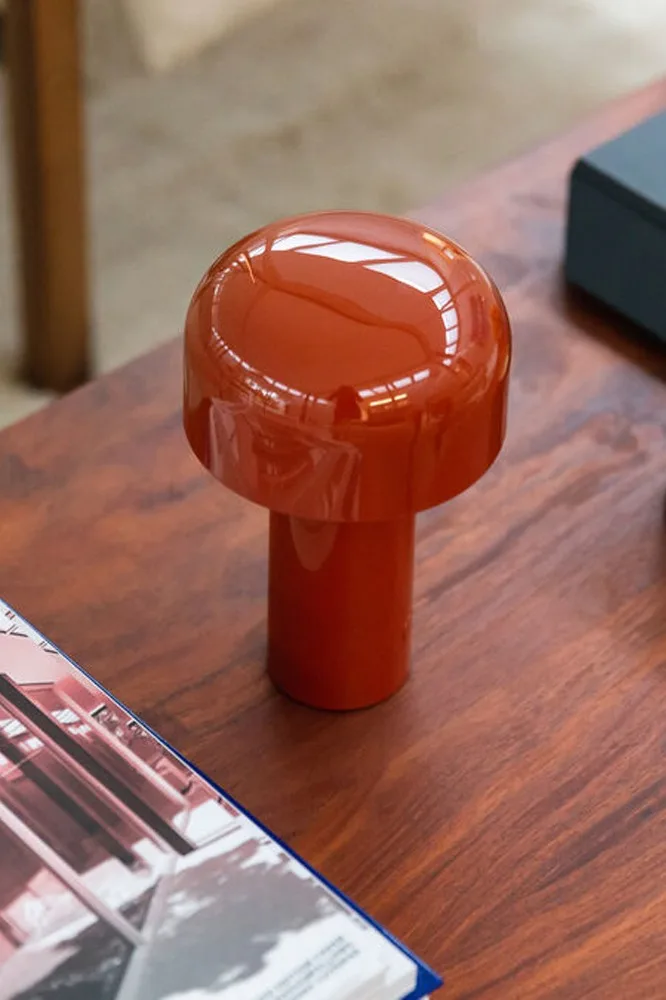 Lampe orange brillante en forme de champignon posée sur une table en bois, avec un magazine au premier plan.