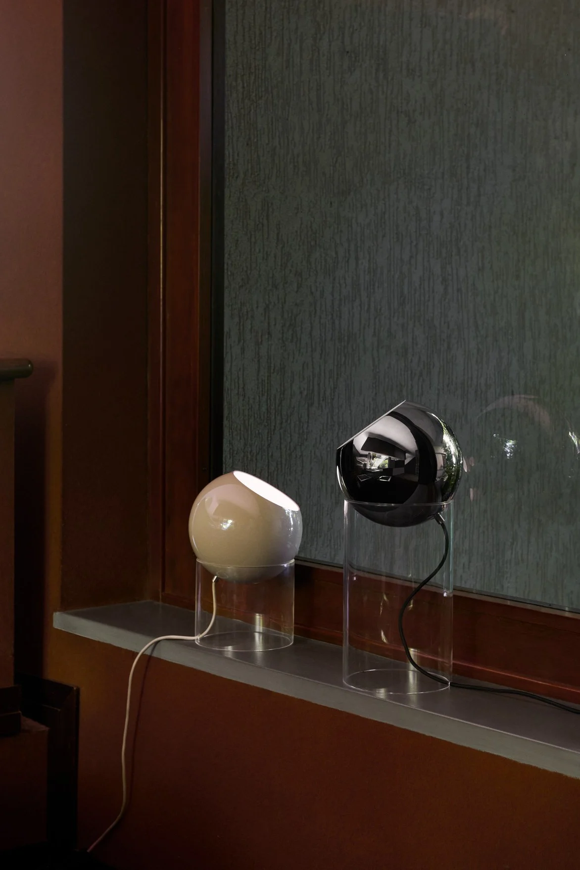 Sur un rebord de fenêtre se trouvent deux lampes de table Topan de différentes tailles, de couleur beige et noire, de la marque &Tradition.