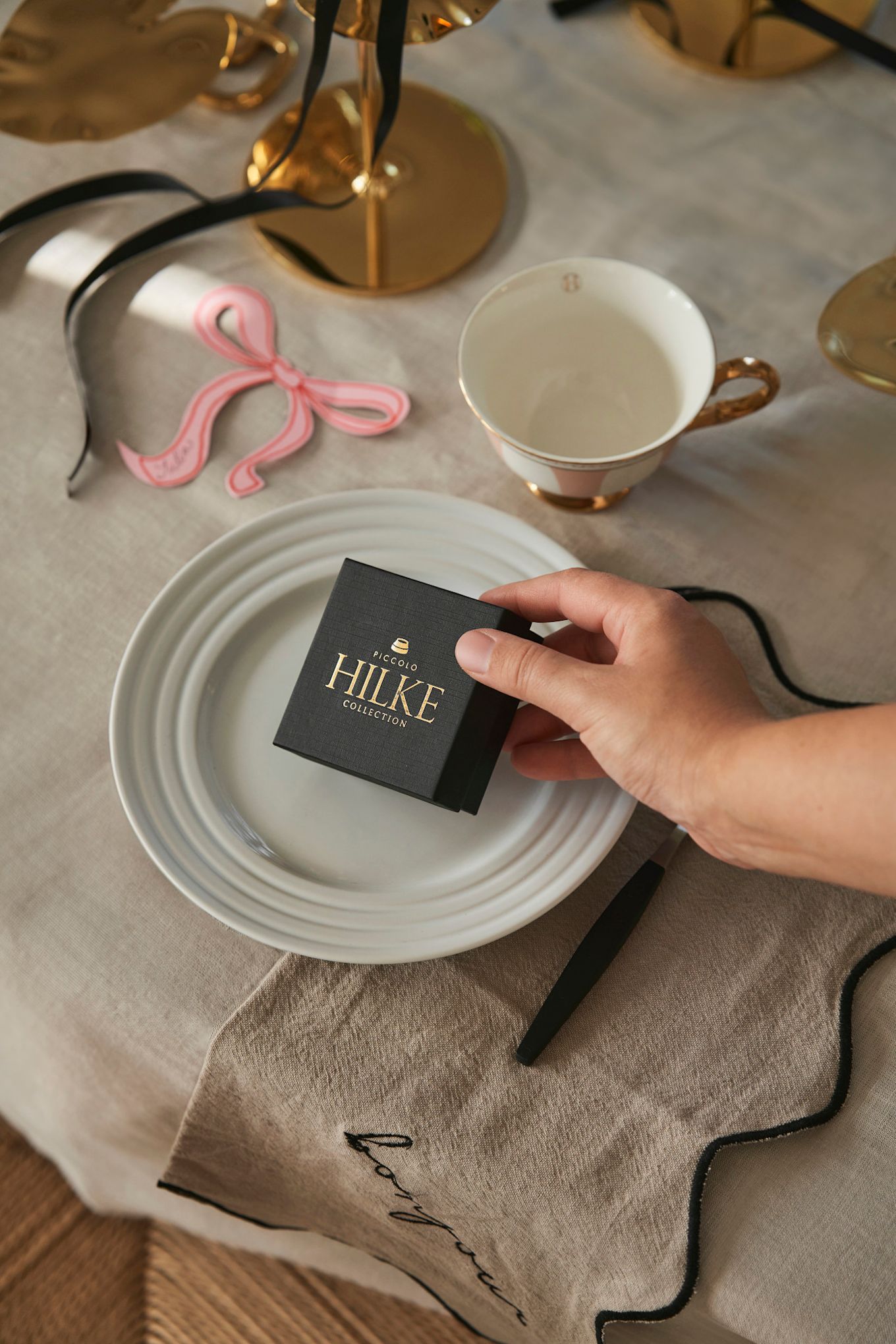 Célébrez la fête de la Galentine chez vous avec vos invit�és préférés. Ici, une main dépose une boîte de la collection Hilke sur un couvert, comme petit cadeau pour vos invités. 