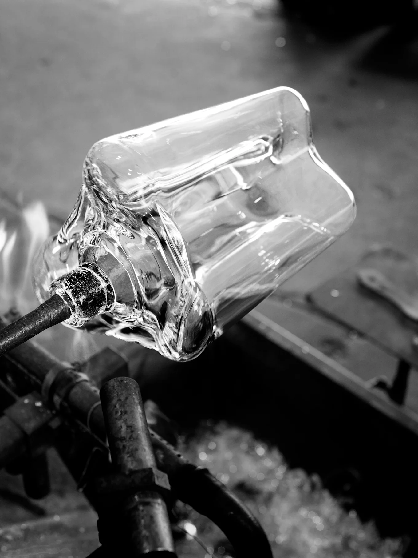 Vase en verre clair façonné sur une tige métallique avec chaleur, noir et blanc.