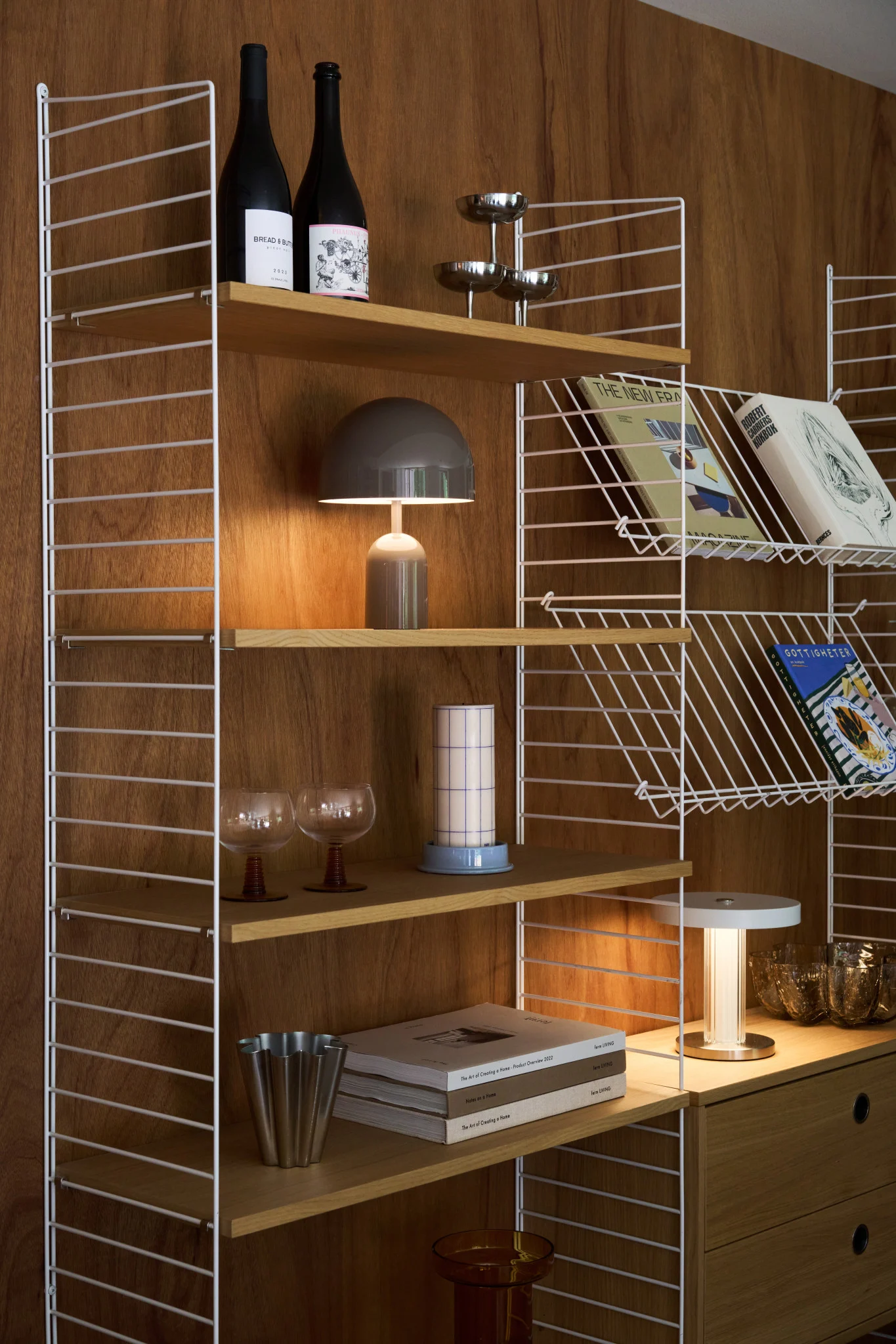 Étagère murale en bois élégante, cadres blancs, avec livres, bouteilles, lampe champignon et objets décoratifs.