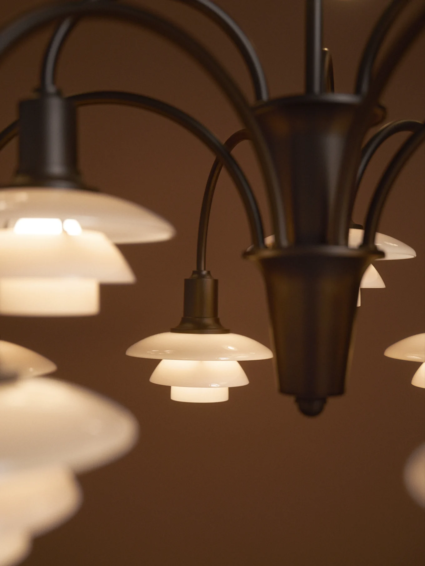 Lustre avec plusieurs abat-jour en verre dépoli étagés et lumineux sur un fond sombre.