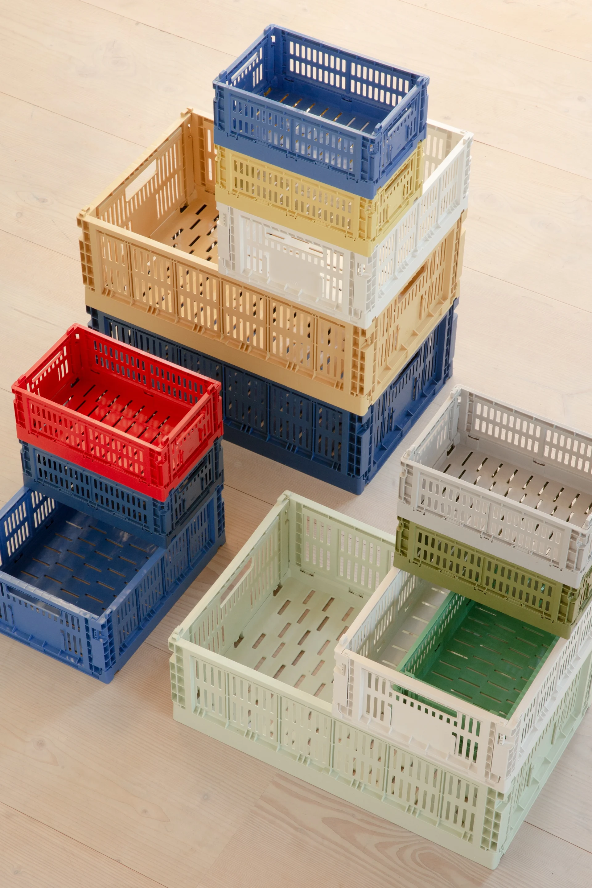Piles de caisses pliantes en plastique colorées et perforées sur un parquet clair.