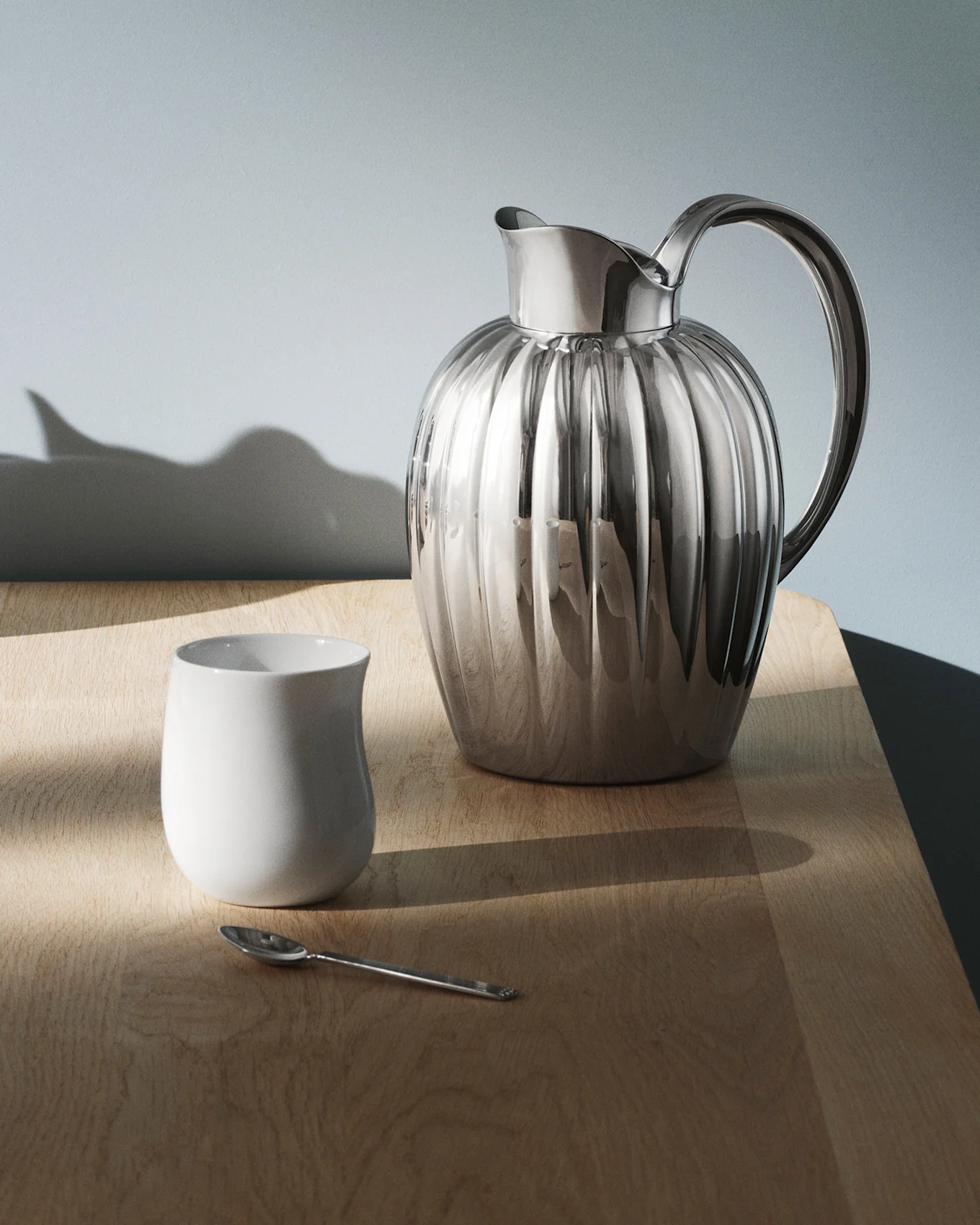 Une cruche en argent brillante et nervurée avec une anse sur une table sombre et réfléchissante, avec des motifs de lumière.