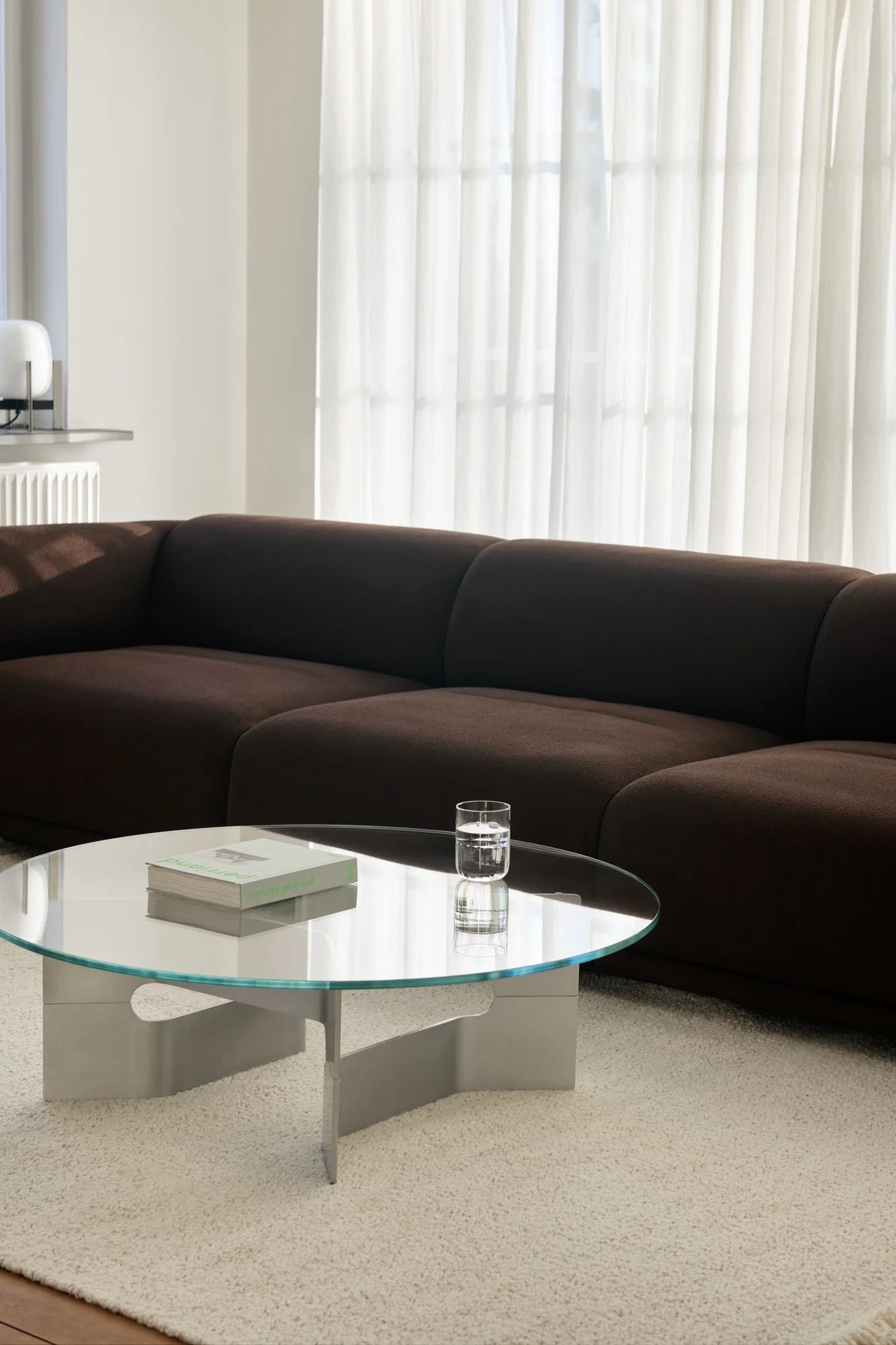 Salon moderne avec un canapé modulable marron foncé, une table basse ronde en verre et un tapis à poils longs de couleur claire.