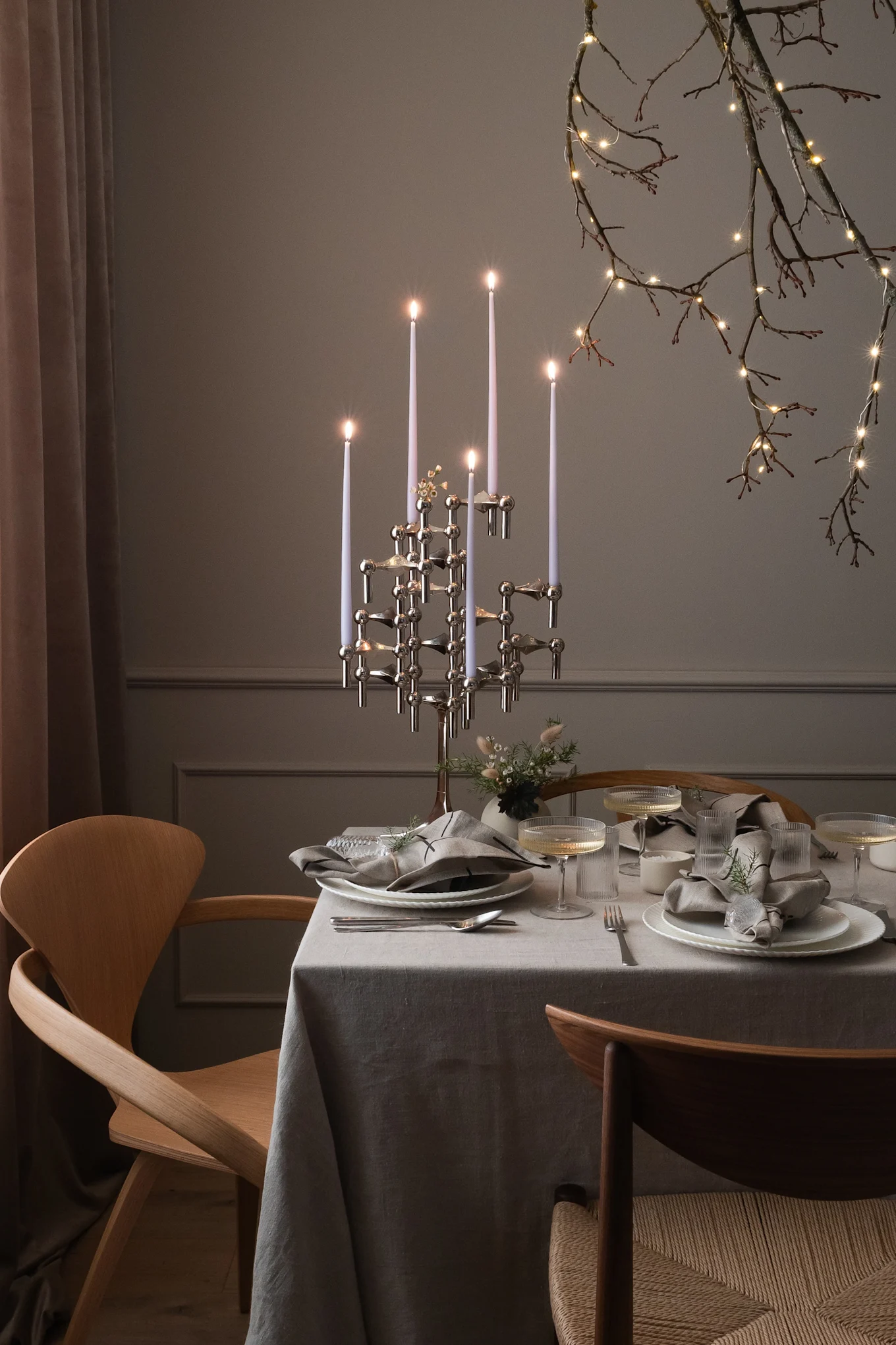 Une table dressée pour une occasion spéciale, avec un candélabre moderne, des couverts et des branches illuminées.