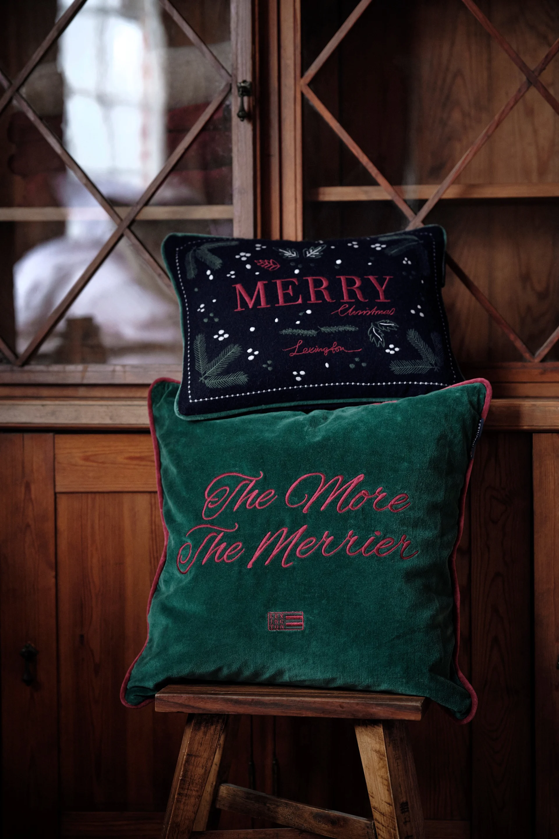 Les coussins sont une décoration de Noël très populaire en 2025 : voici deux coussins festifs de Lexington posés sur un tabouret.