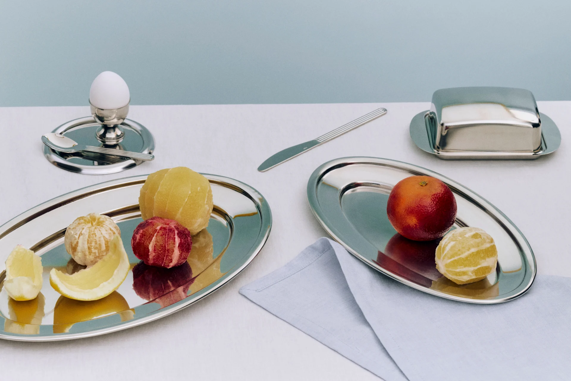 Petit déjeuner avec agrumes pelés et non pelés sur des plateaux en argent, un œuf et un beurrier.