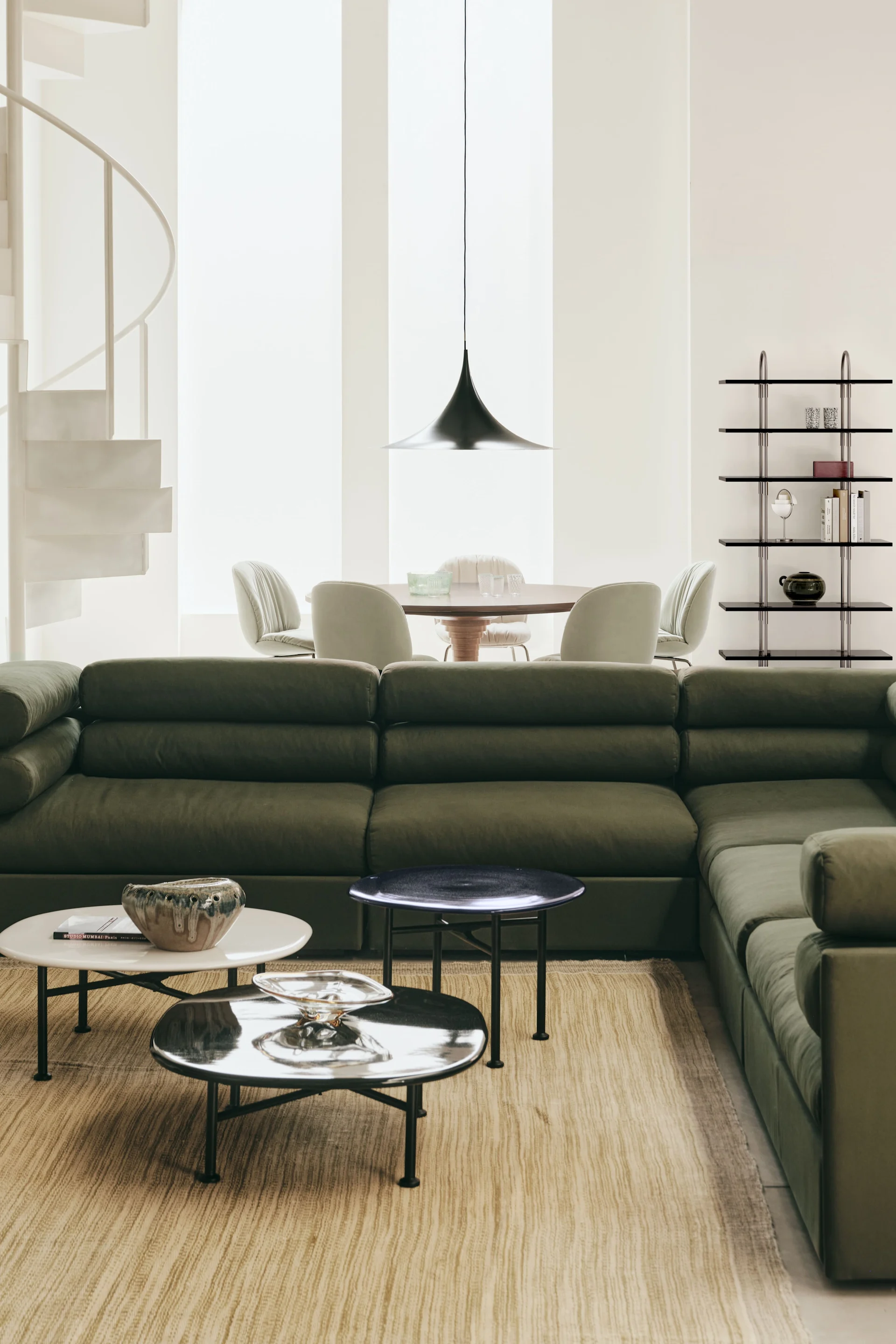 Le plafonnier idéal pour le salon : ici, la suspension Semi de Gubi est suspendue dans un salon aménagé avec des meubles verts.