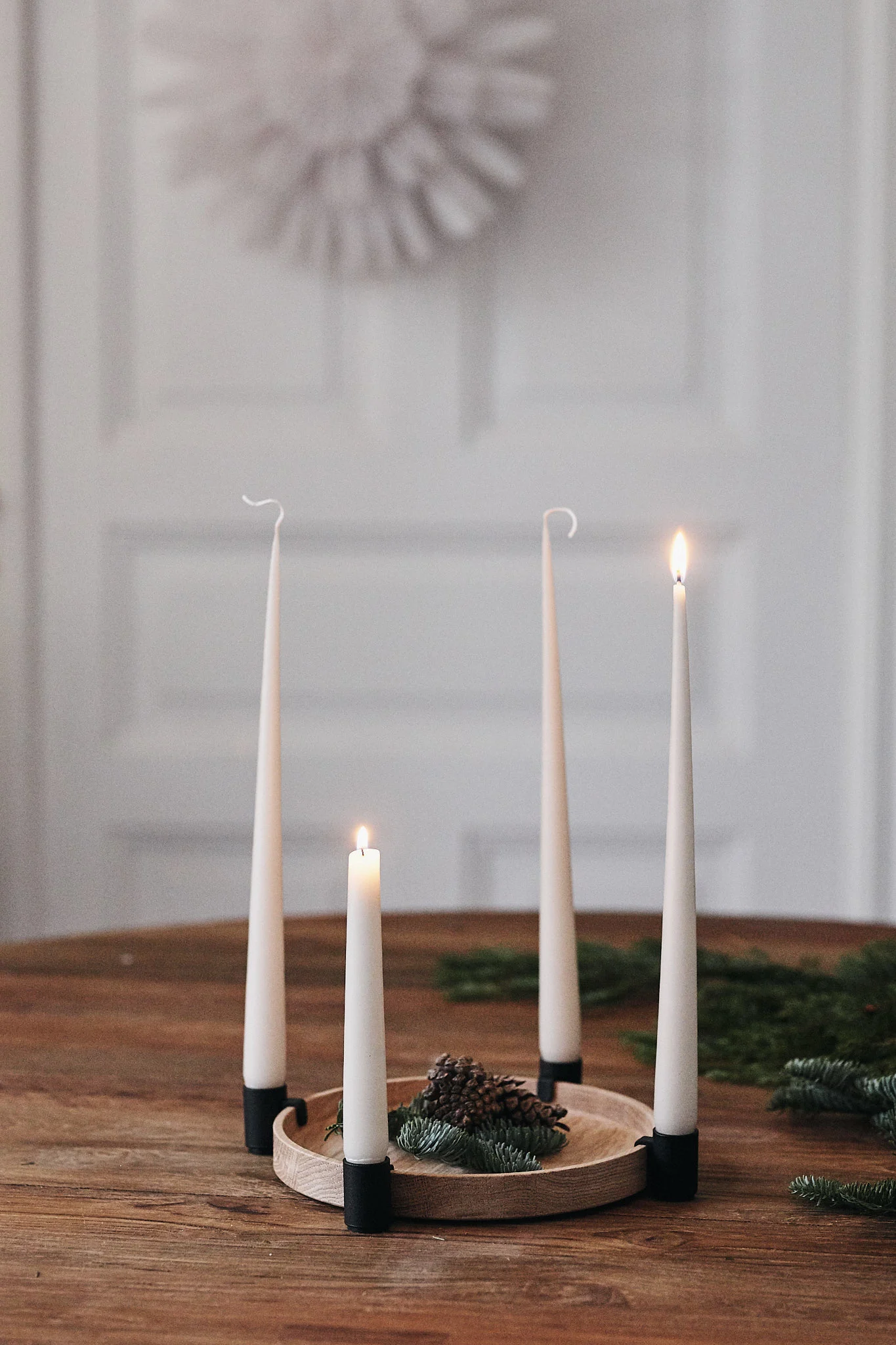Un bougeoir rond de l'Avent avec quatre bougies est posé sur une table et deux des bougies sont allumées.