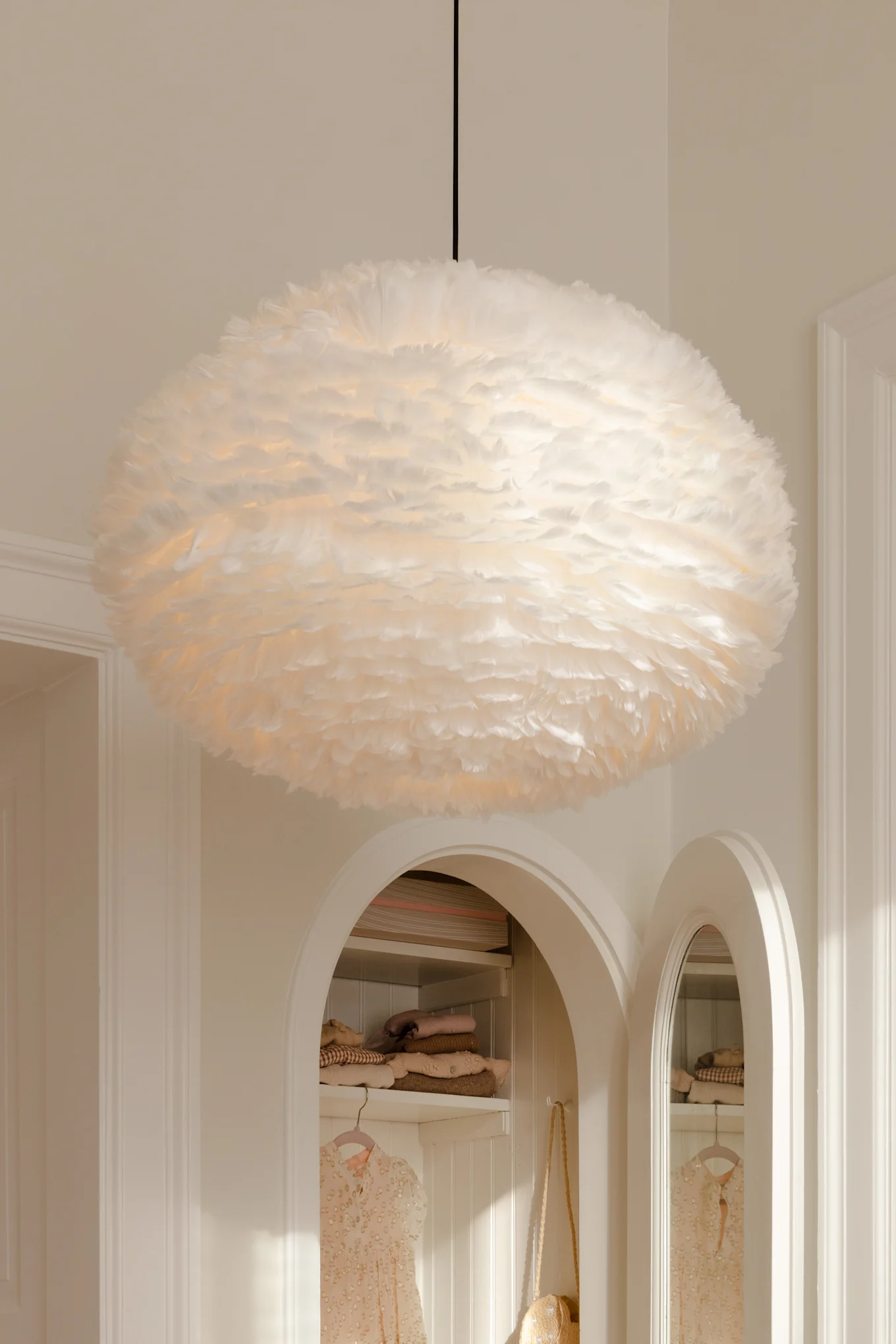 Une grande suspension blanche et duveteuse en plumes pend du plafond au-dessus de niches cintrées avec des vêtements.
