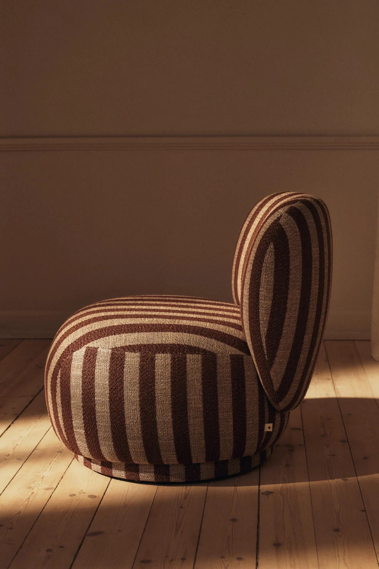 Fauteuil arrondi avec des rayures marron et beige sur un parquet en bois.