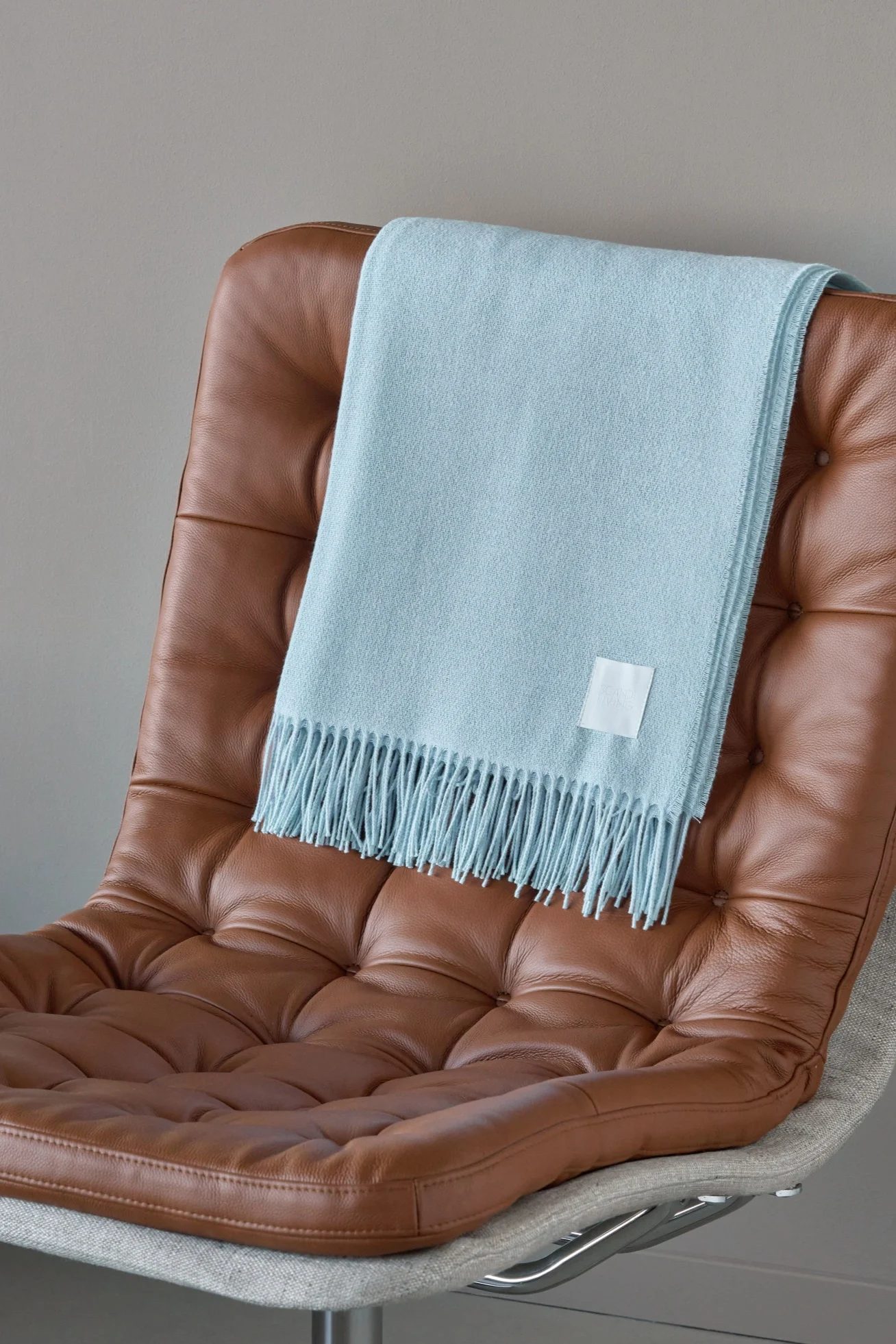 Une couverture bleu clair à franges drapée sur un fauteuil en cuir marron.