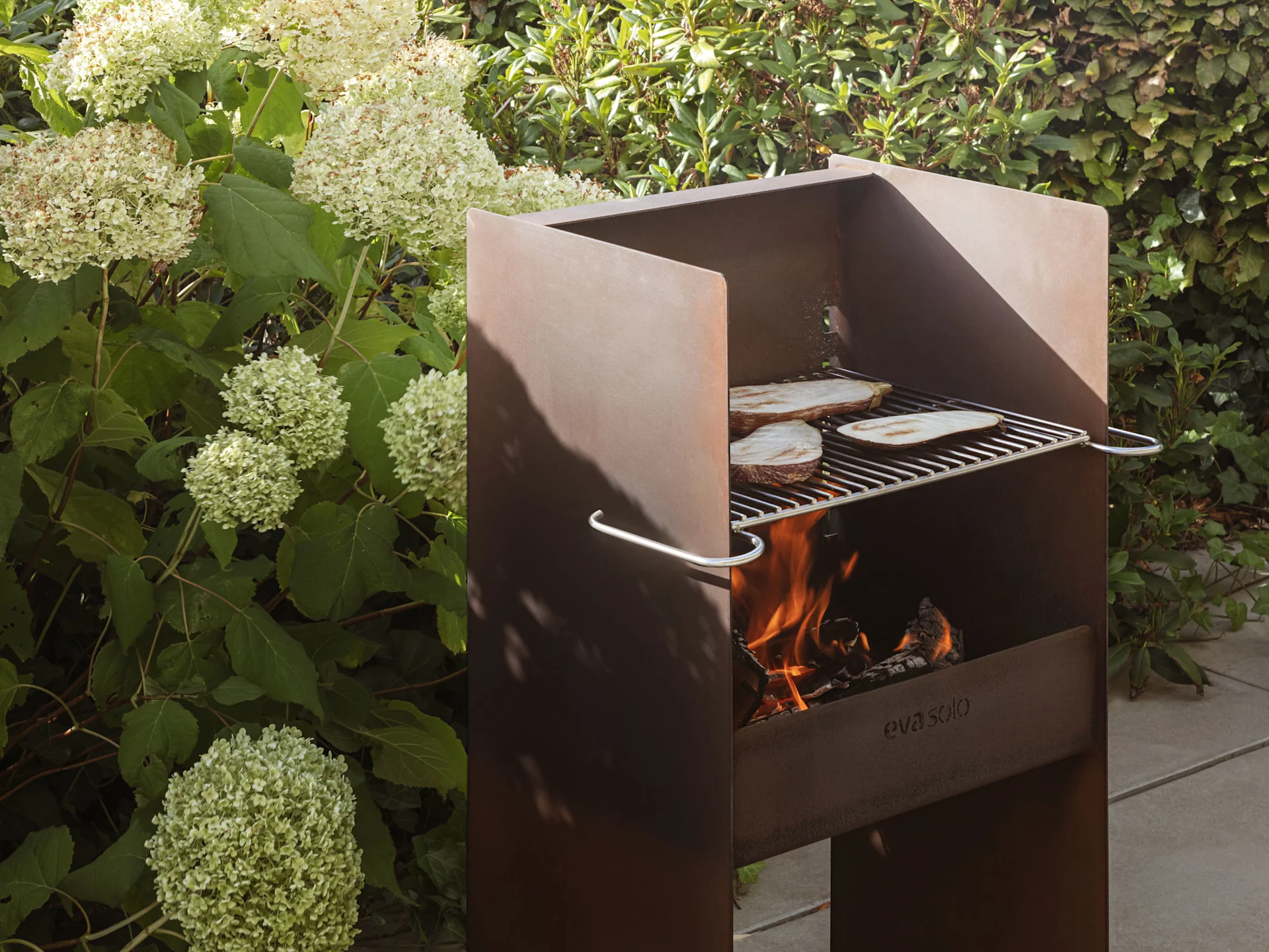 Un barbecue extérieur en métal rustique avec des flammes et des tranches d'aubergine cuisant sur la grille.