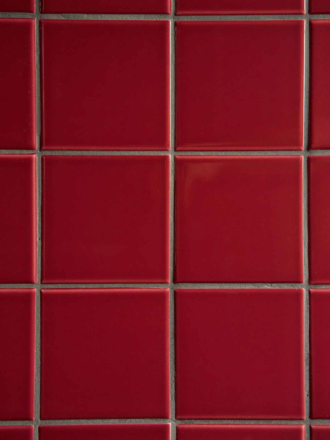 Une grille de carreaux rouges carrés brillants avec des joints gris foncé.