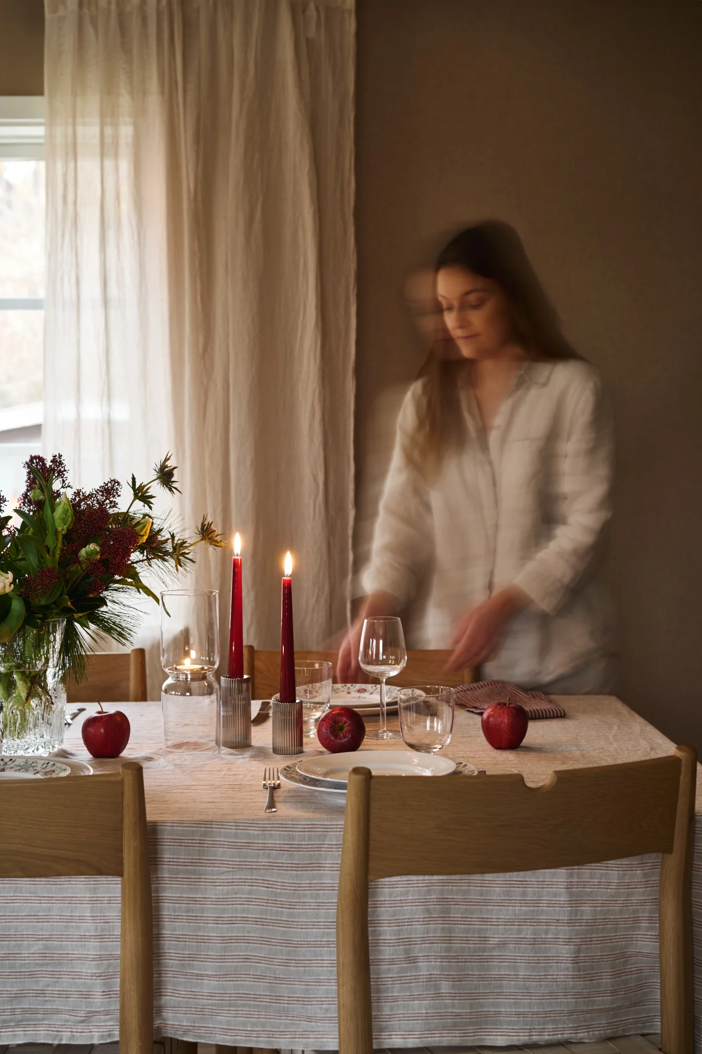 Une femme dresse une table de Noël simple avec des bougies rouges, de la porcelaine de Noël à motifs et une simple nappe rayée. 