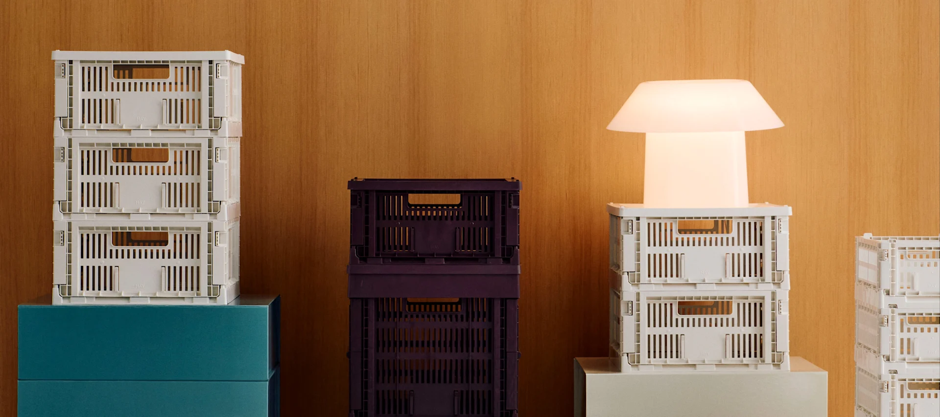 Piles de caisses pliantes blanches et violet foncé avec une lampe moderne blanche lumineuse sur un fond en bois.