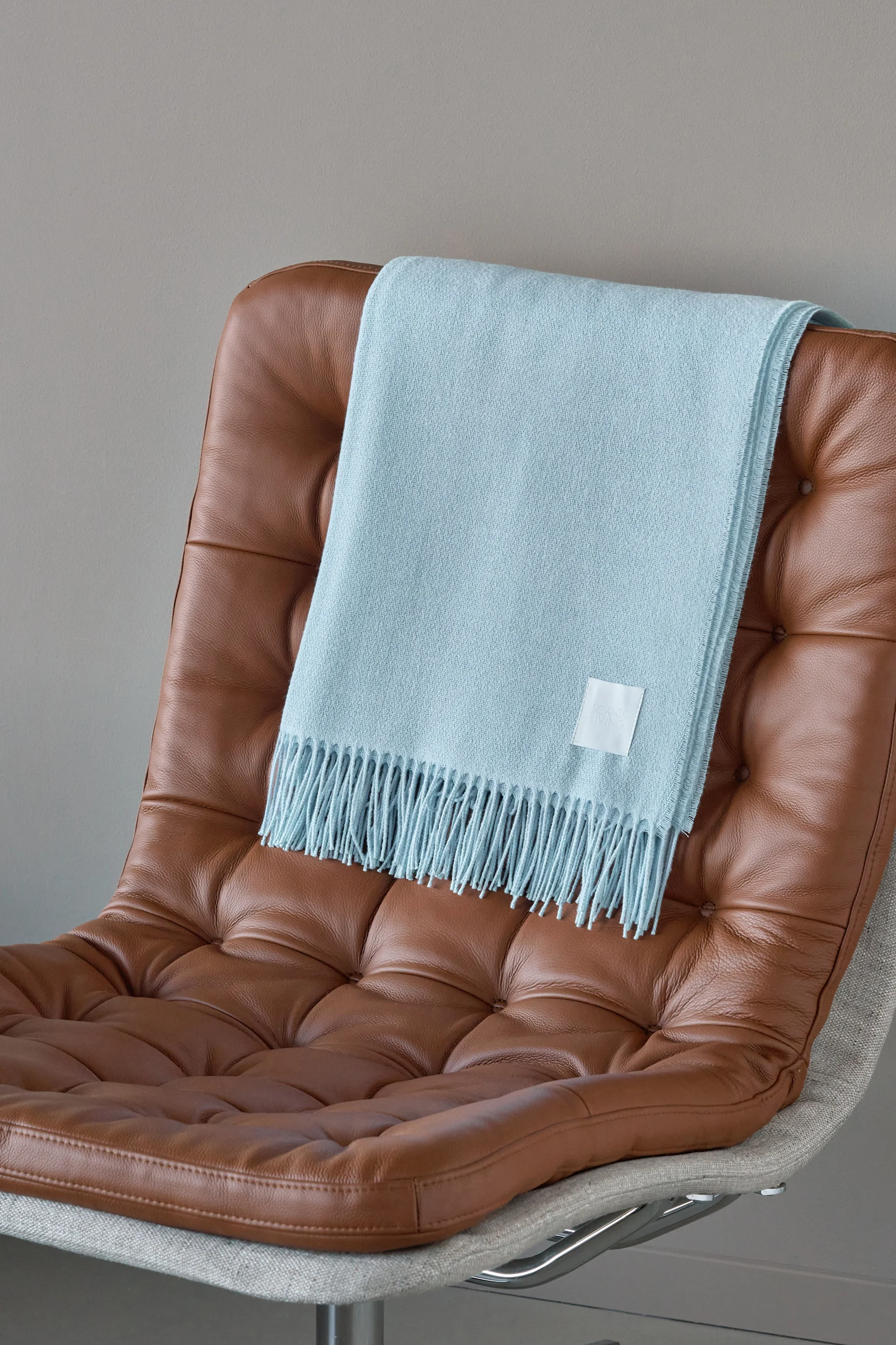 Plaid bleu clair à franges drapé sur un fauteuil en cuir marron capitonné.