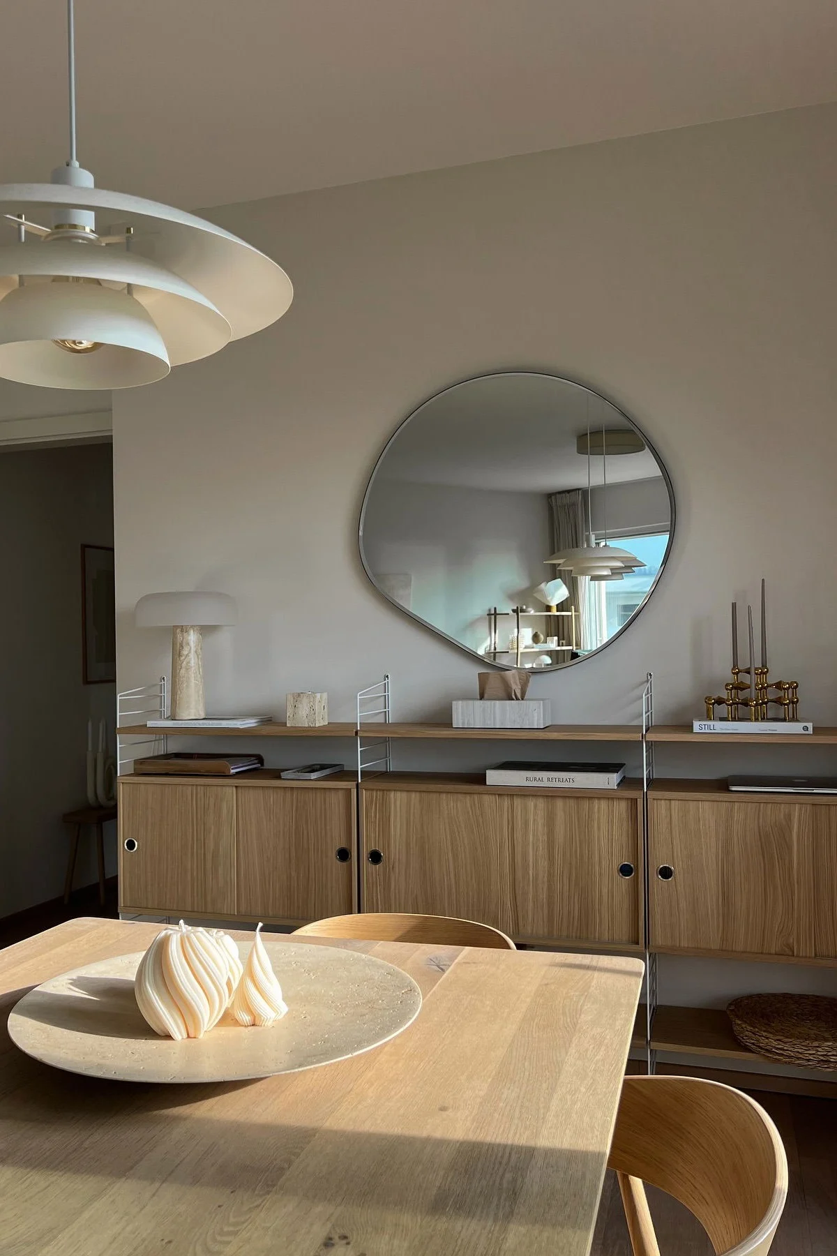 Salle à manger moderne: table en bois, deux bougies spirales, étagère, miroir irrégulier et lampe étagée.