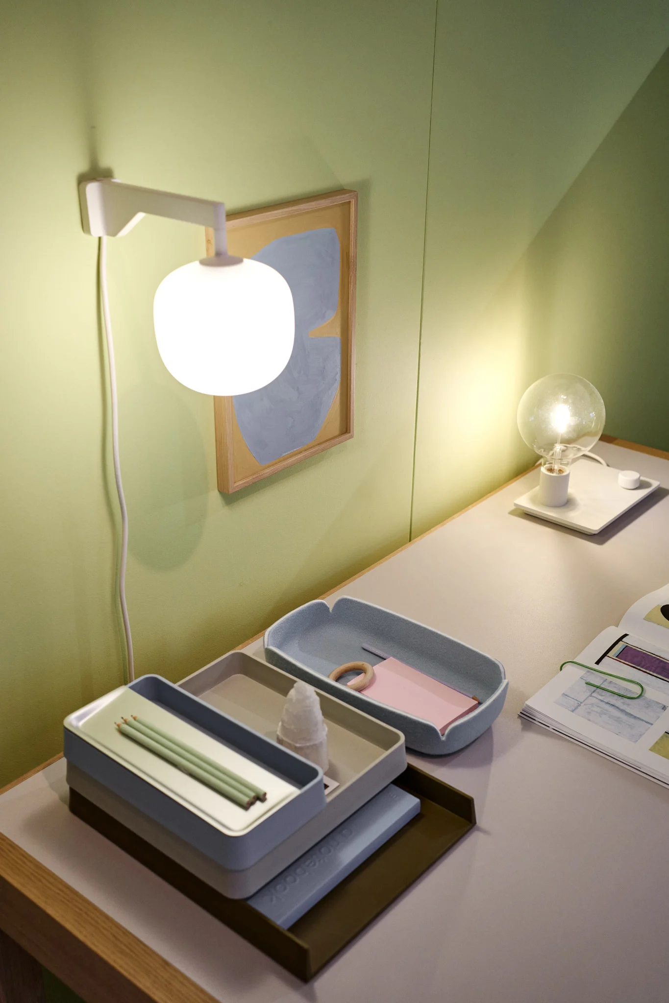 Un bureau bien rangé devant un mur vert grâce à l'applique beige Rime de Muuto.