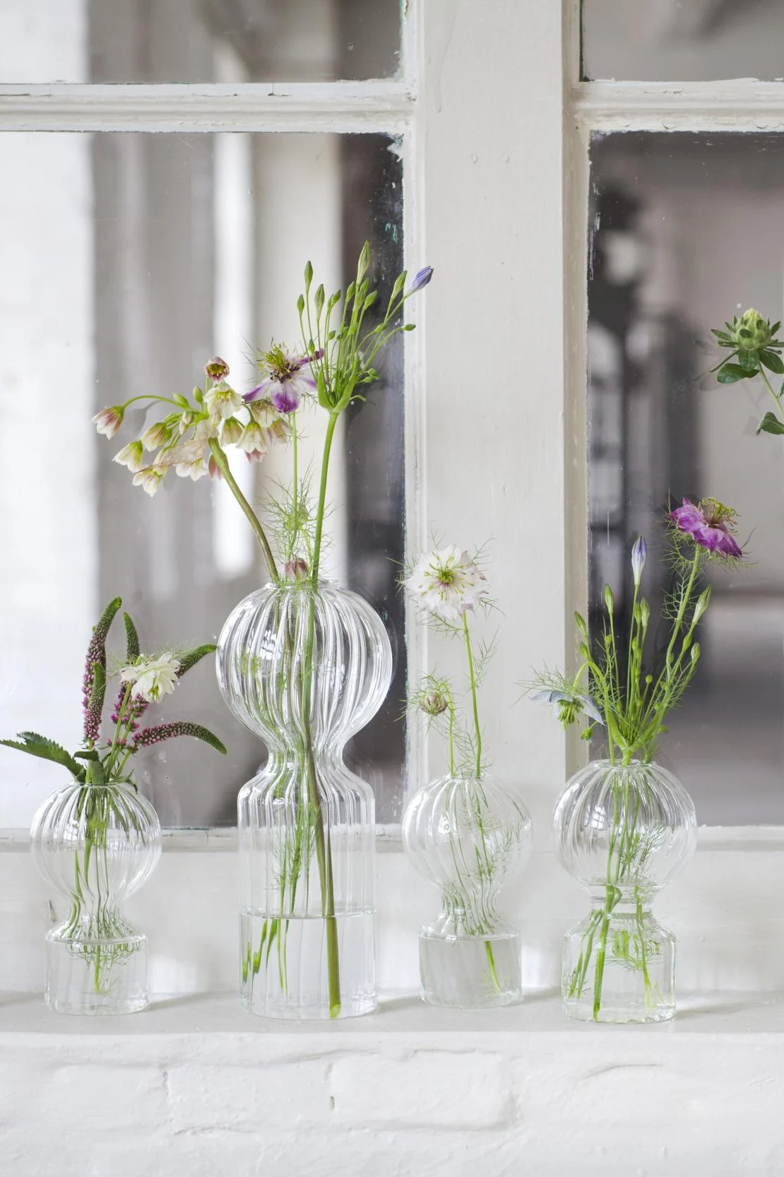 Sur un rebord de fenêtre sont posés les trois mini-vases Iki Doll de Serax contenant chacun une tige.