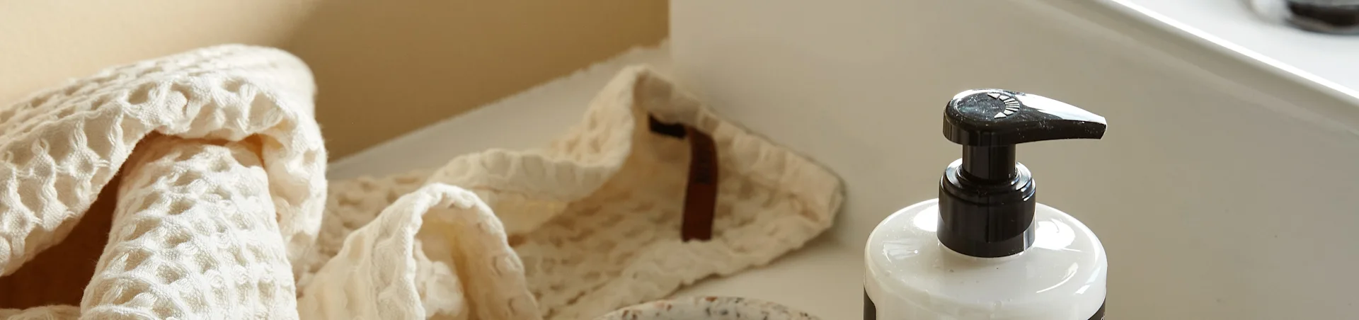 Une serviette gaufrée de couleur claire pliée à côté d'une bouteille à pompe blanche sur une surface propre et claire.