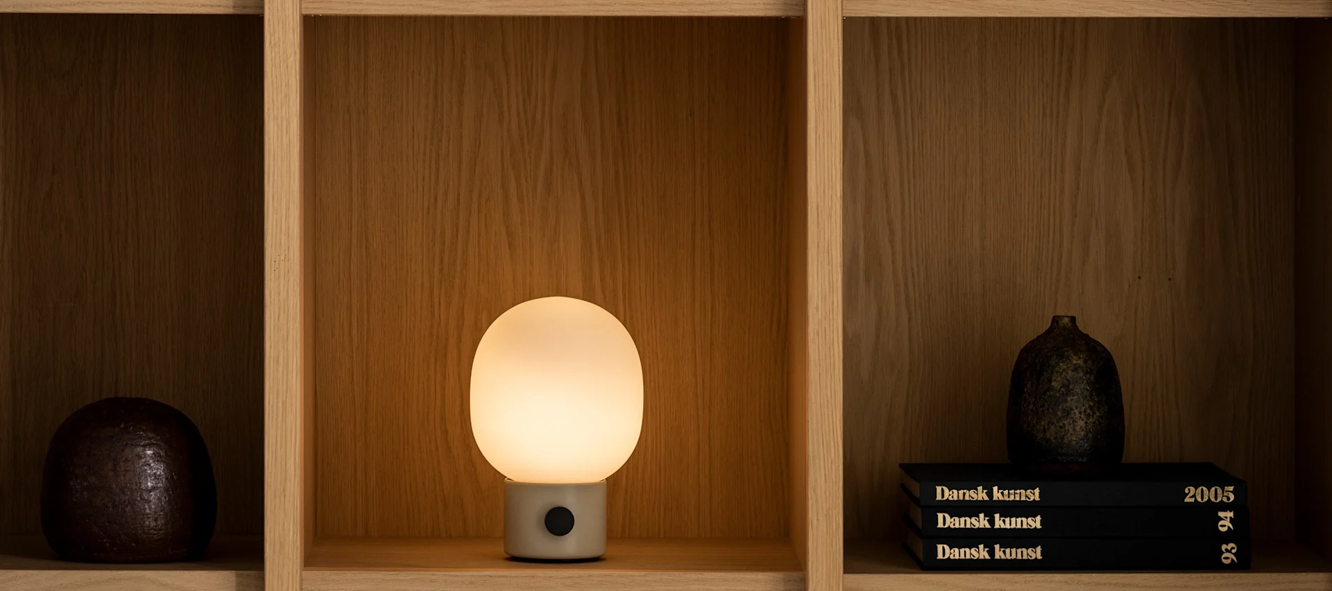 Une lampe de table JWDA lumineuse d'Audo Copenhagen trône sur une étagère.