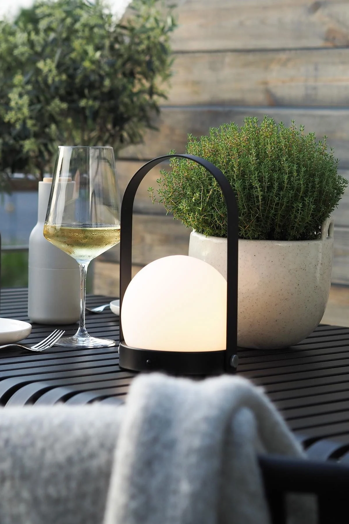 La lampe portable Carrie d'Audo Copenhagen et le pot de fleurs Speckle de Ferm Living sont posés sur la table Palissade de HAY sur la terrasse de @wohngluecksieben.
