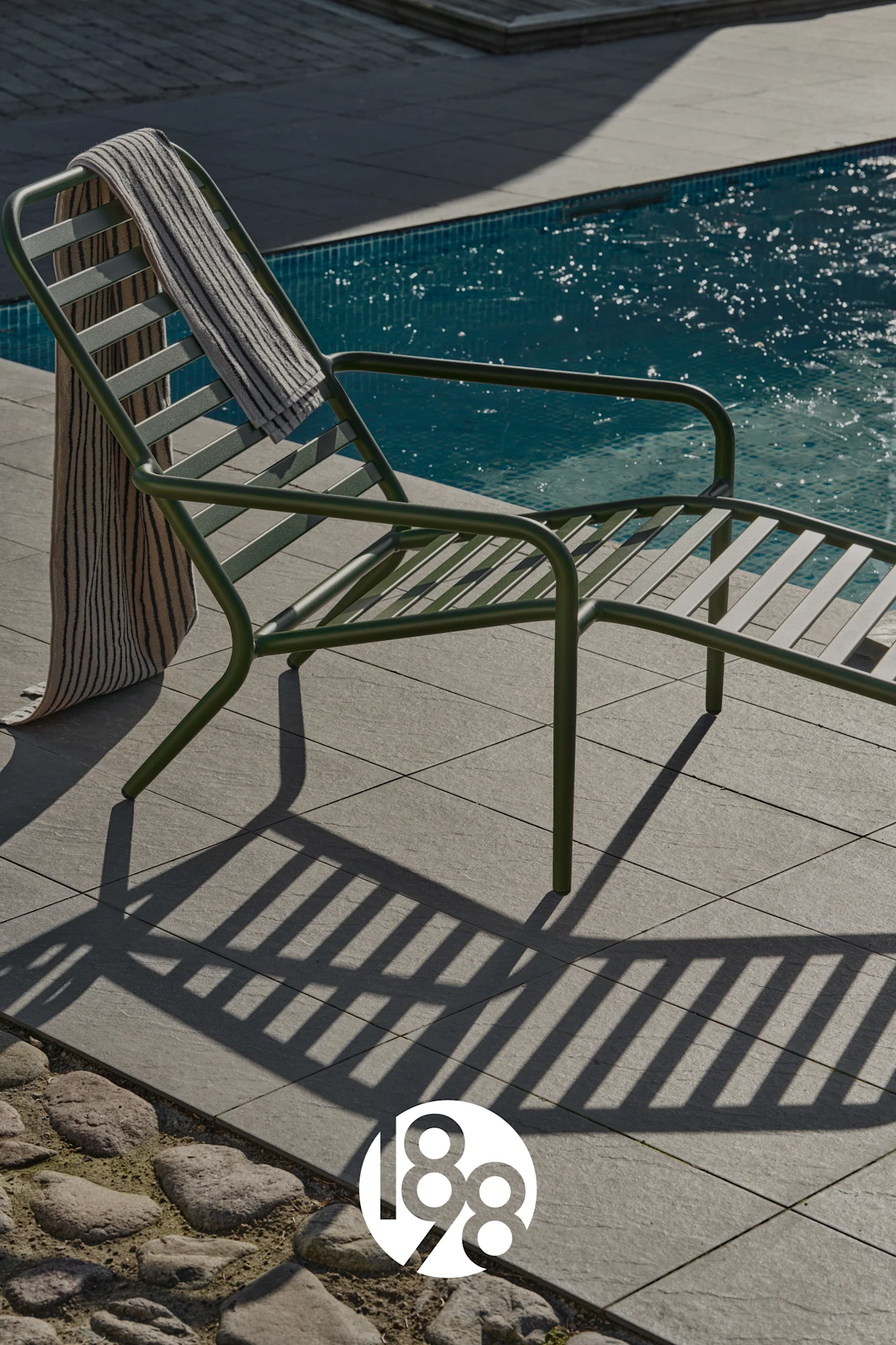 Chaise longue vert foncé avec une serviette rayée près d'une piscine bleue.