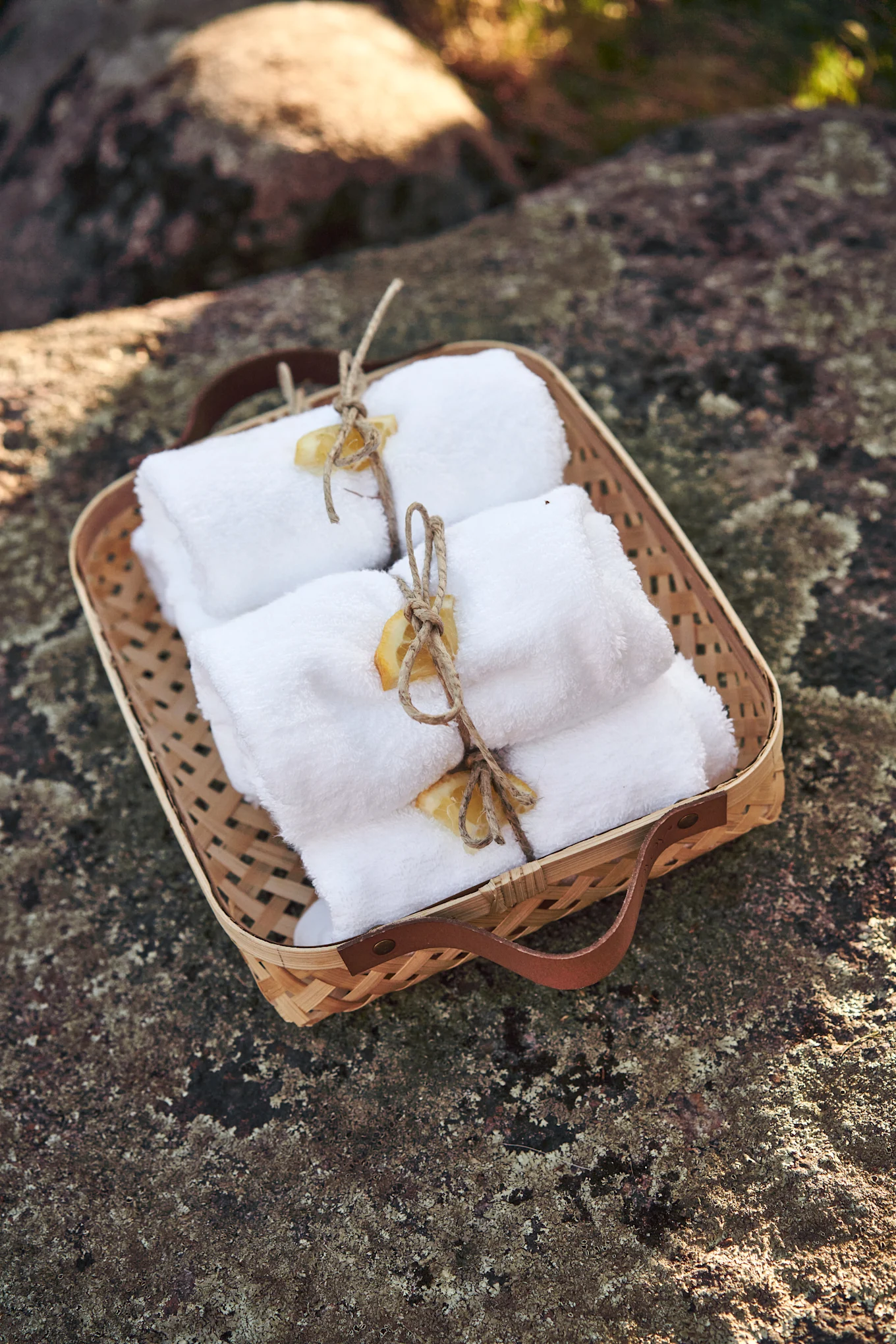Panier tressé contenant des serviettes blanches roulées attachées avec de la ficelle et des tranches d'agrumes séchées sur une roche texturée.