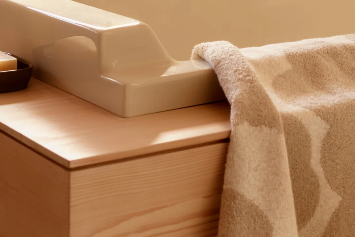Gros plan d'une serviette beige texturée drapée sur un accessoire en céramique clair sur une vanité en bois avec un savon.
