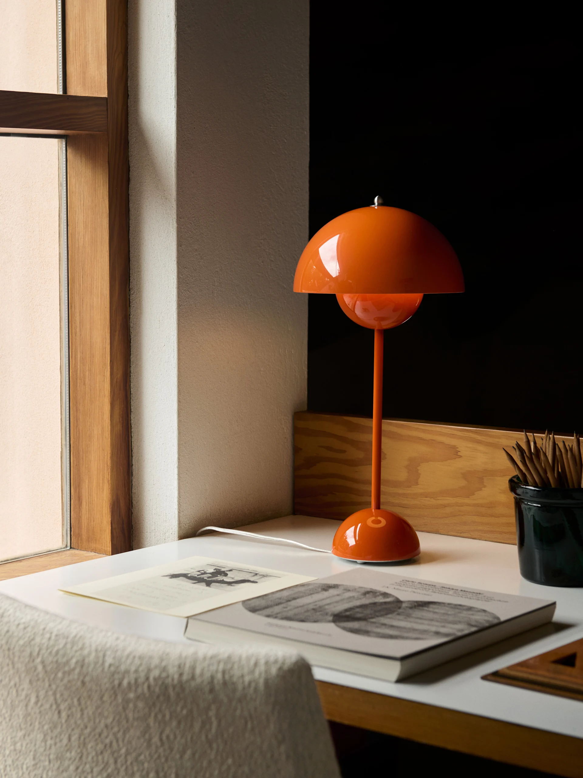 Une lampe de table orange en forme de dôme repose sur un bureau blanc à côté de livres et d'un pot à crayons.