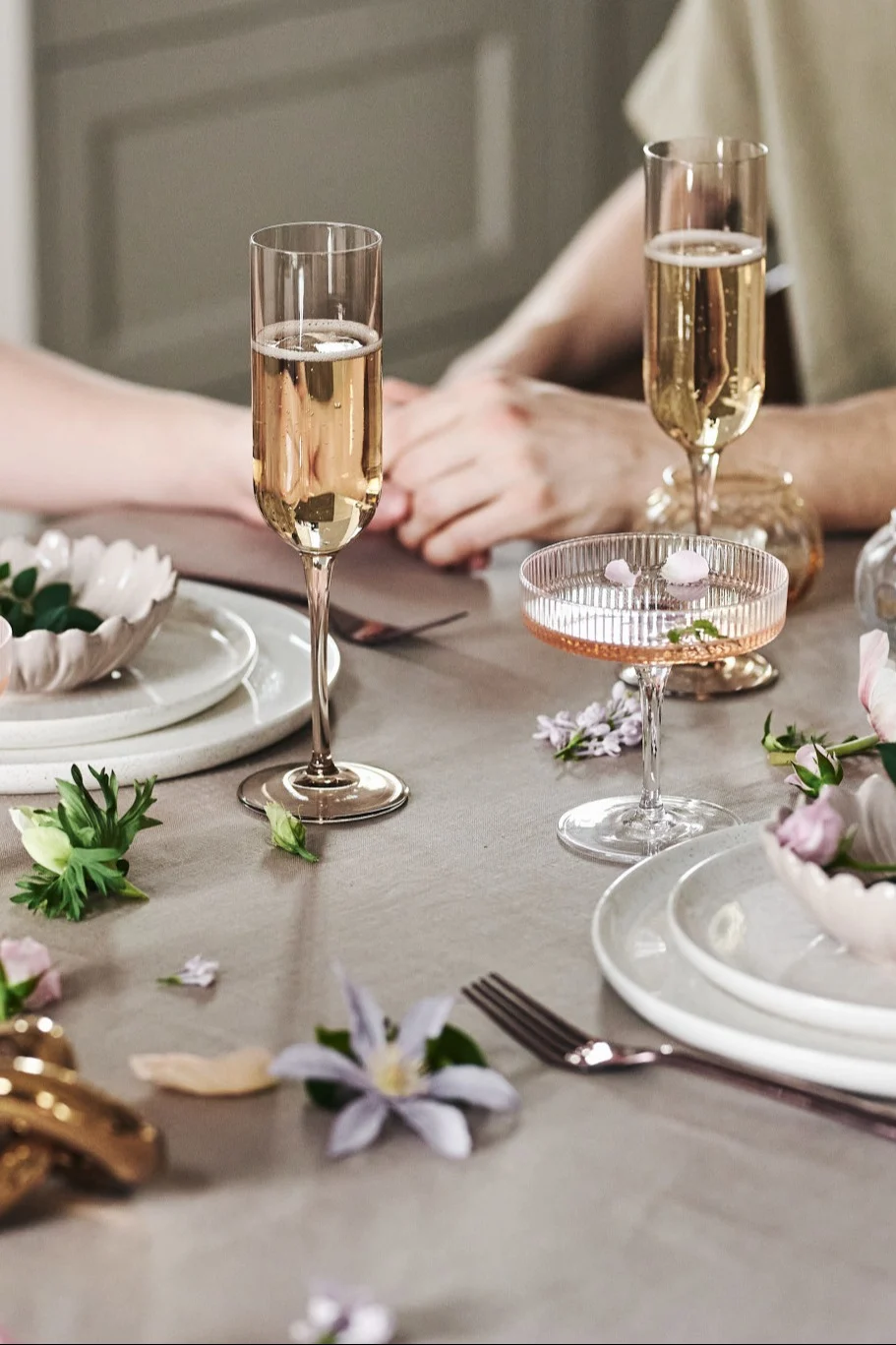 Vous pouvez également décorer la table de manière ludique pour votre repas romantique à la maison. Ici, vous voyez de la vaisselle blanche, des verres simples et des fleurs sur une nappe beige.
