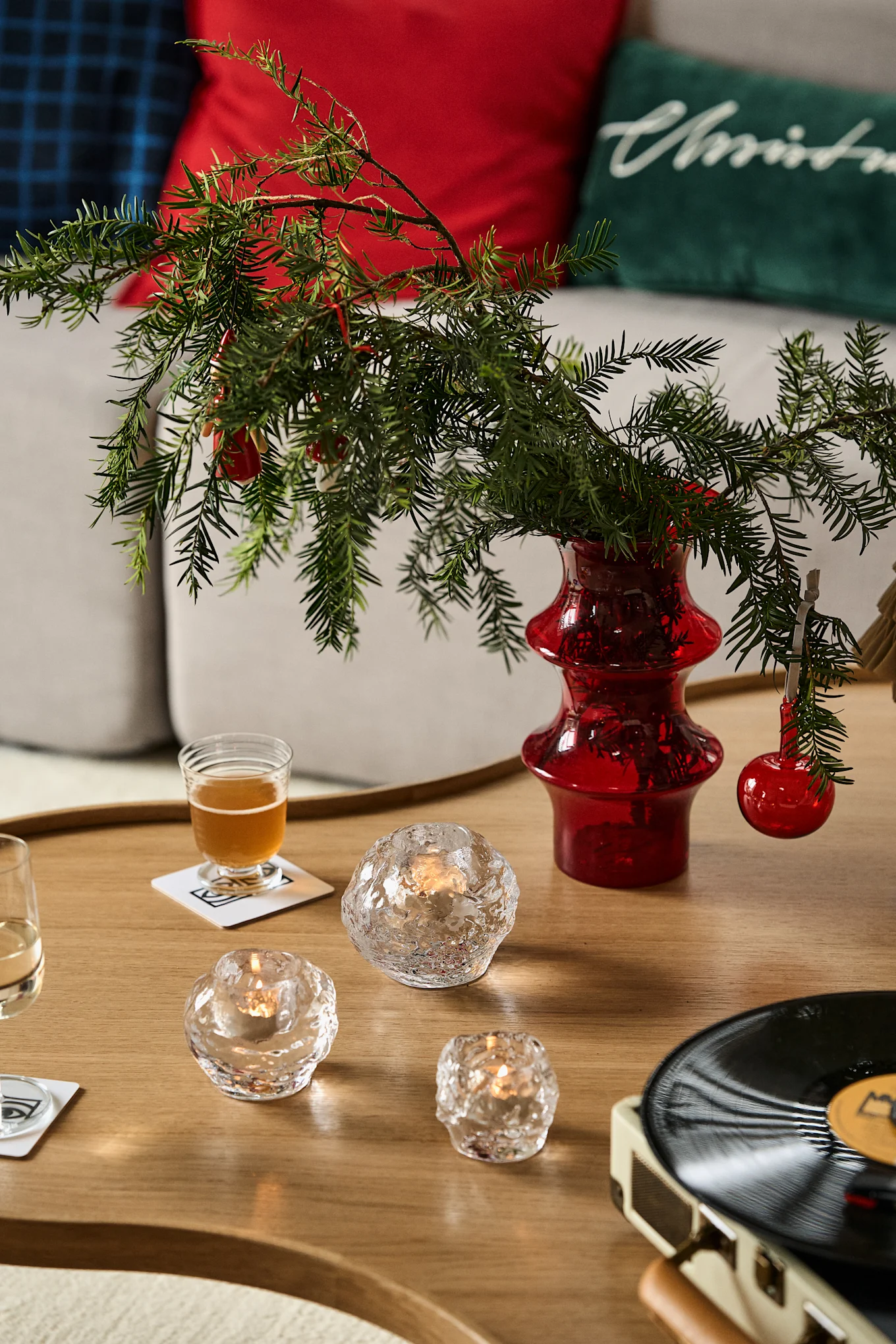 Idées cadeaux pour Noël : vous voyez ici une table en bois avec un vase contenant des branches de sapin, devant laquelle sont disposés trois photophores de la collection Snowball de Kosta Boda.