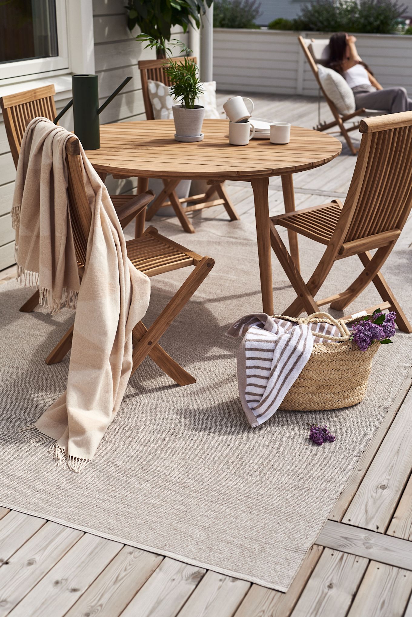 Une terrasse avec des meubles en bois, par exemple l'ensemble de balcon Aneboda de 1898 et le tapis en coton Rime de Scandi Living sur le tapis en plastique Mellow.