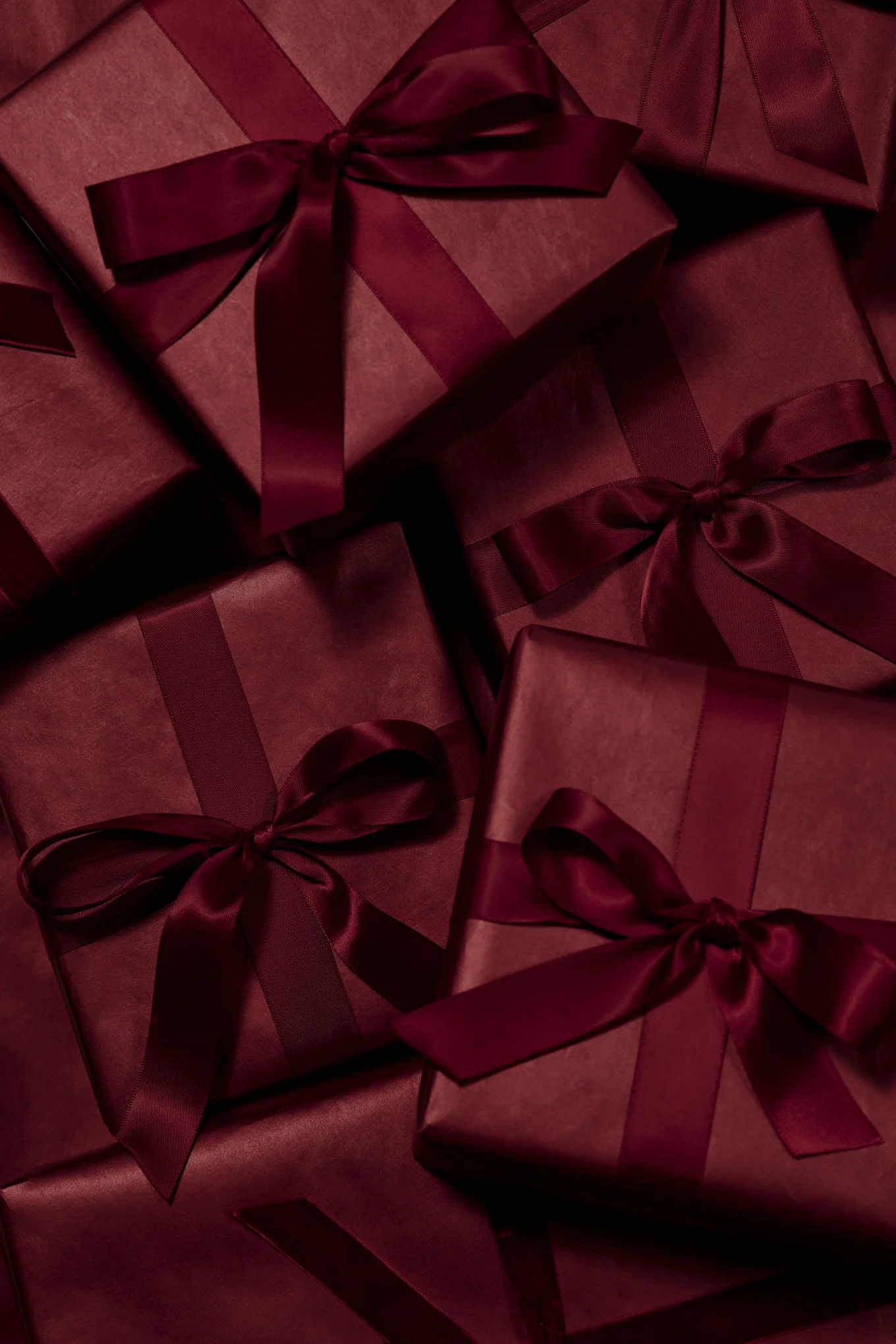 Plusieurs boîtes cadeaux rouge foncé emballées avec des rubans et des nœuds en satin assortis.