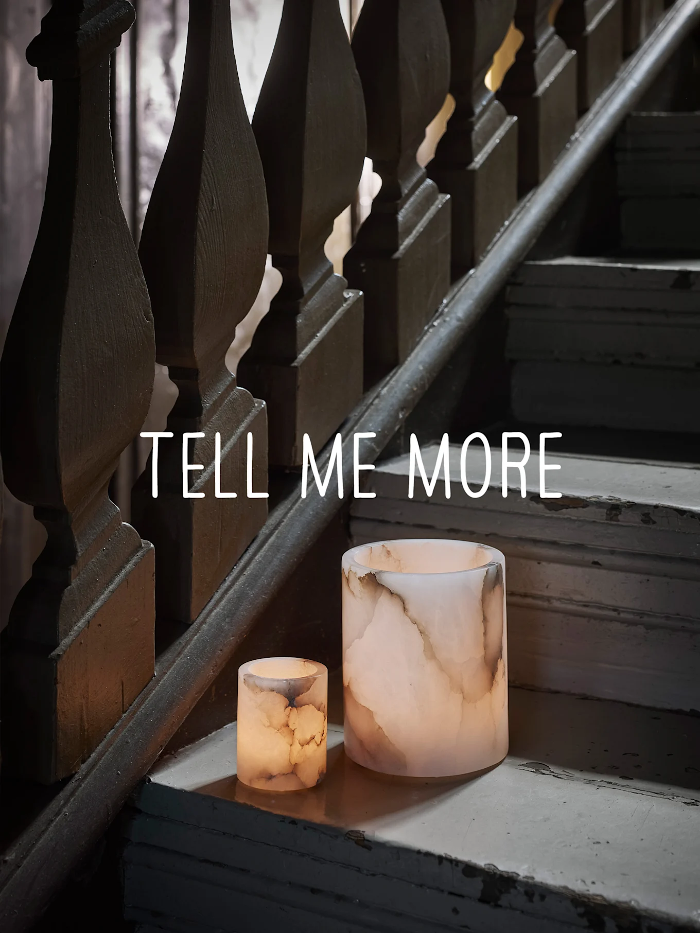 Deux bougeoirs lumineux en onyx sur un escalier en bois usé, avec le texte "TELL ME MORE".