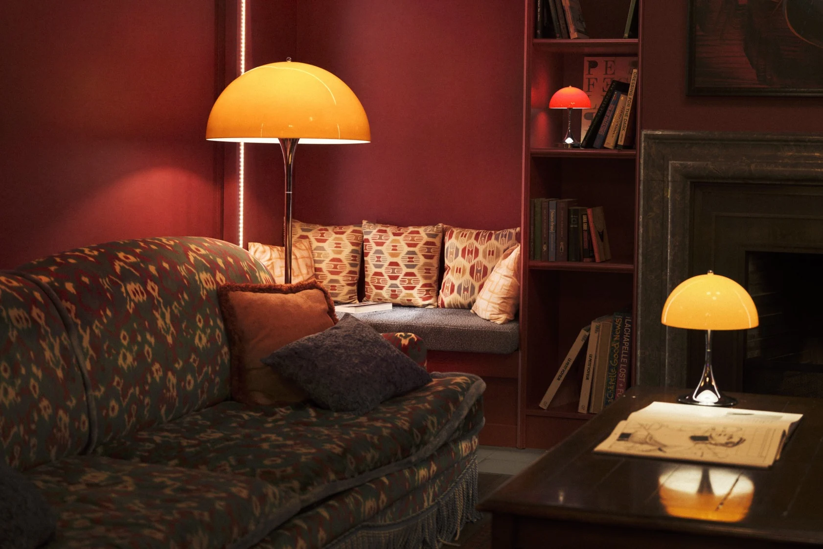 Un lampadaire de style rétro avec un abat-jour dôme orange et un pied chromé éclaire une pièce avec un tapis et une armoire en bois.