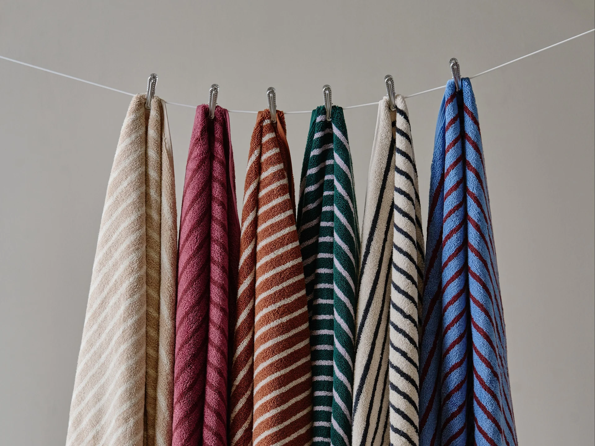 Six serviettes colorées à rayures suspendues à une corde à linge devant un mur uni.