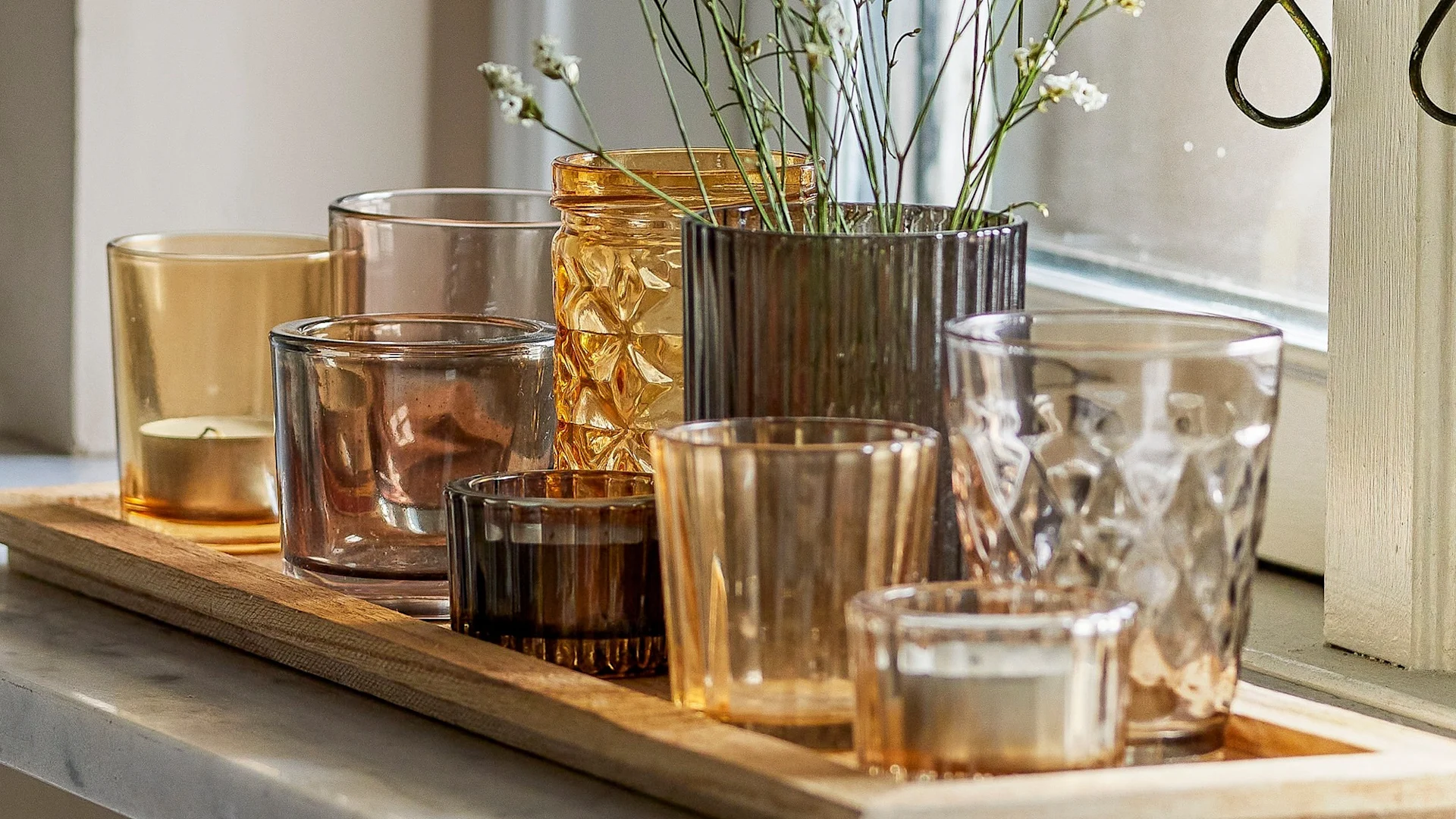 La décoration bohème parfaite : le plateau Sanga avec des porte-bougies chauffe-plat aux différentes teintes de jaune et de brun de Bloomingville est posé sur un rebord de fenêtre.