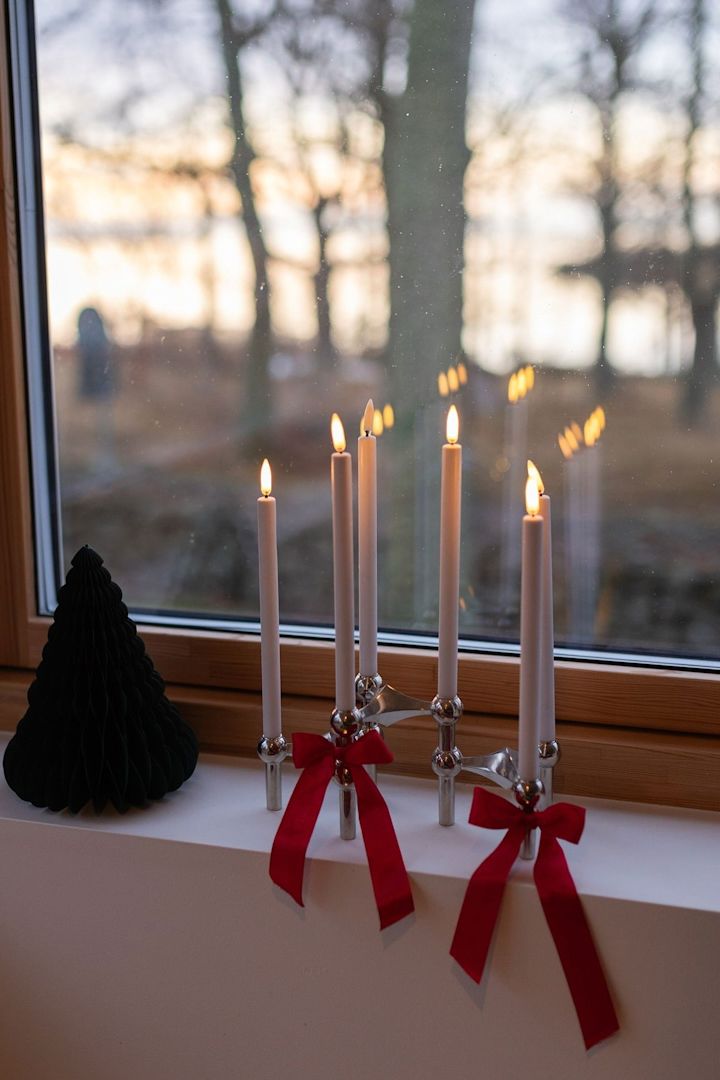 Les nœuds sont très tendance dans les décorations de Noël pour 2025. Nouez-en quelques-uns autour du bougeoir en tissu et placez-le sur le rebord de la fenêtre.