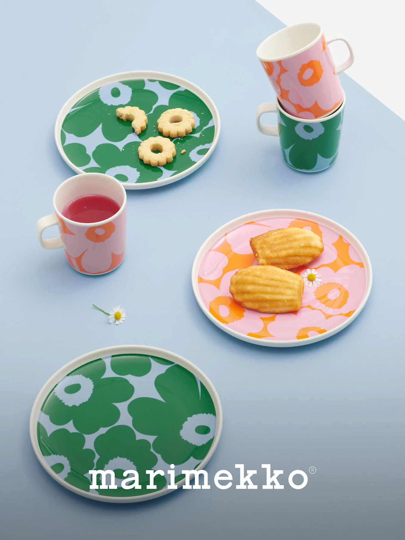 Assiettes et tasses Marimekko aux motifs floraux audacieux en vert, rose et orange, contenant des biscuits, des madeleines et une boisson.