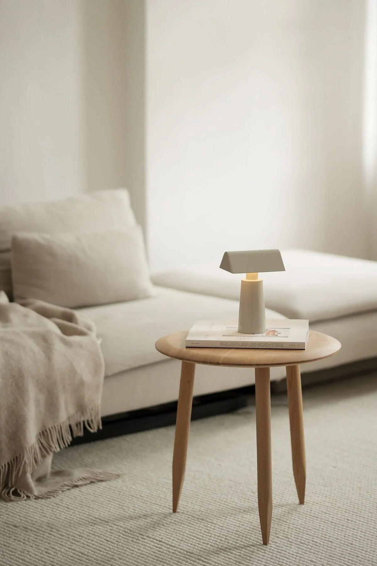 Le style d'habitation Lagom se caractérise par des couleurs discrètes. Ici, vous voyez le salon beige de @b.wohnbar avec un canapé et une table d'appoint devant laquelle se trouve la lampe de table Caret MF1 de &Tradition.