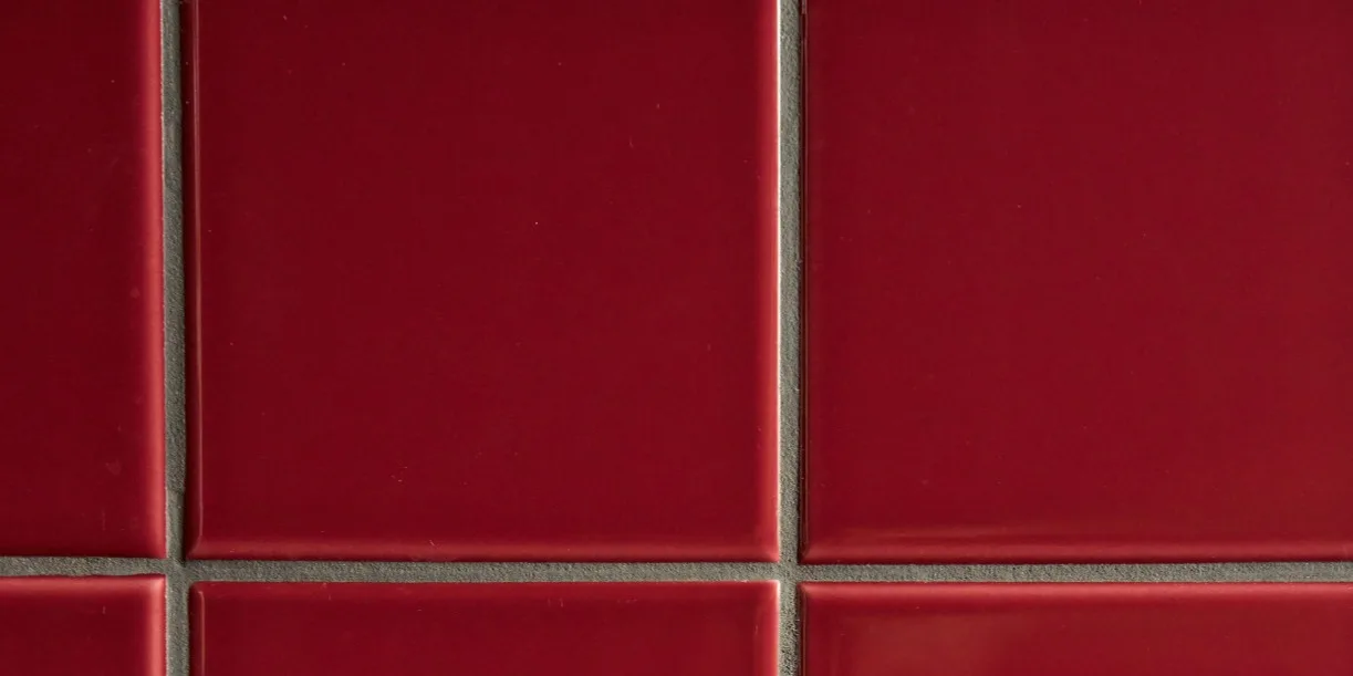 Carreaux carrés rouge foncé brillants avec des joints gris clair dans un motif de grille.