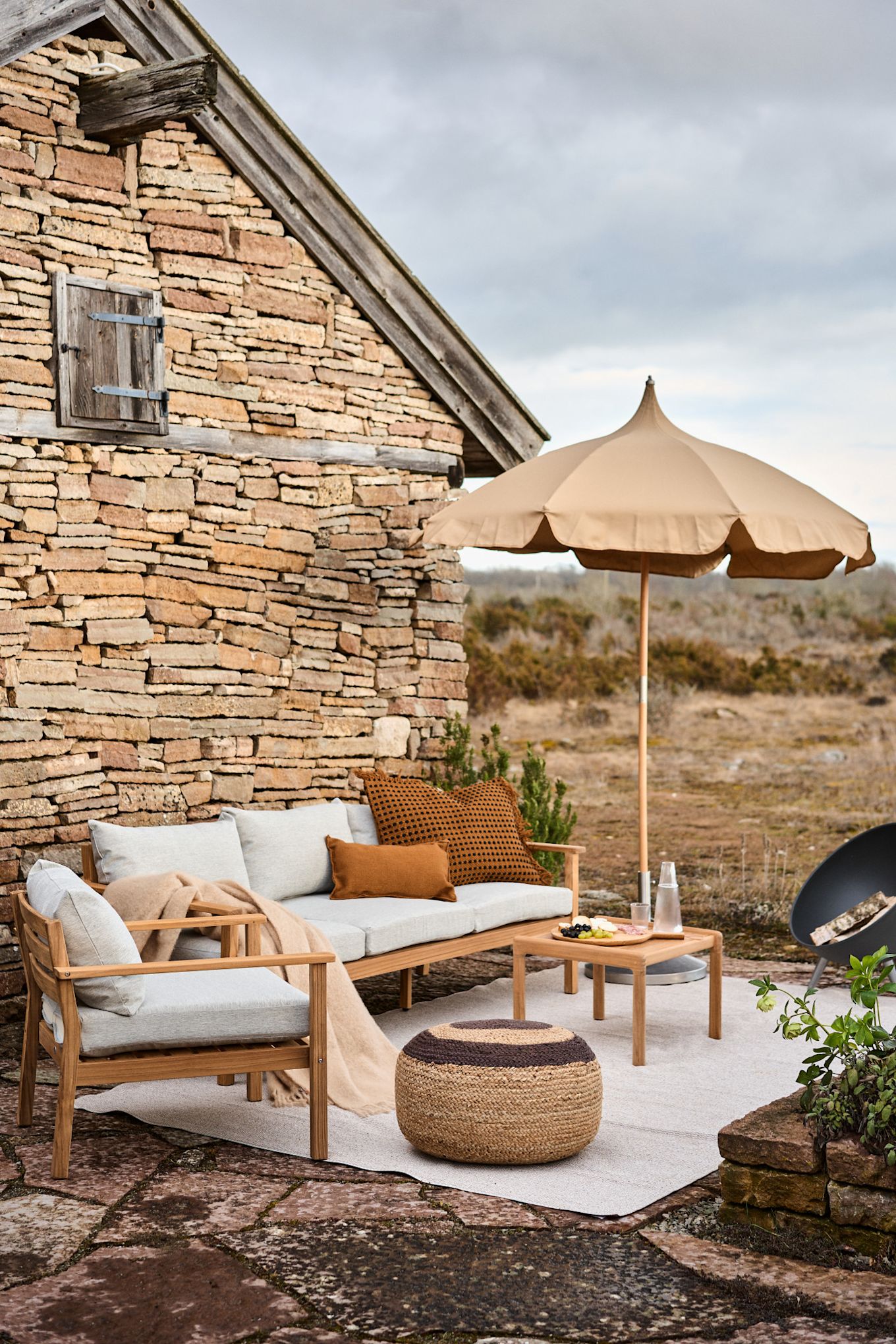 Un coin salon sur une terrasse méditerranéenne avec le parasol beige Lull de Ferm Living et le coussin Melooni de OYOY.