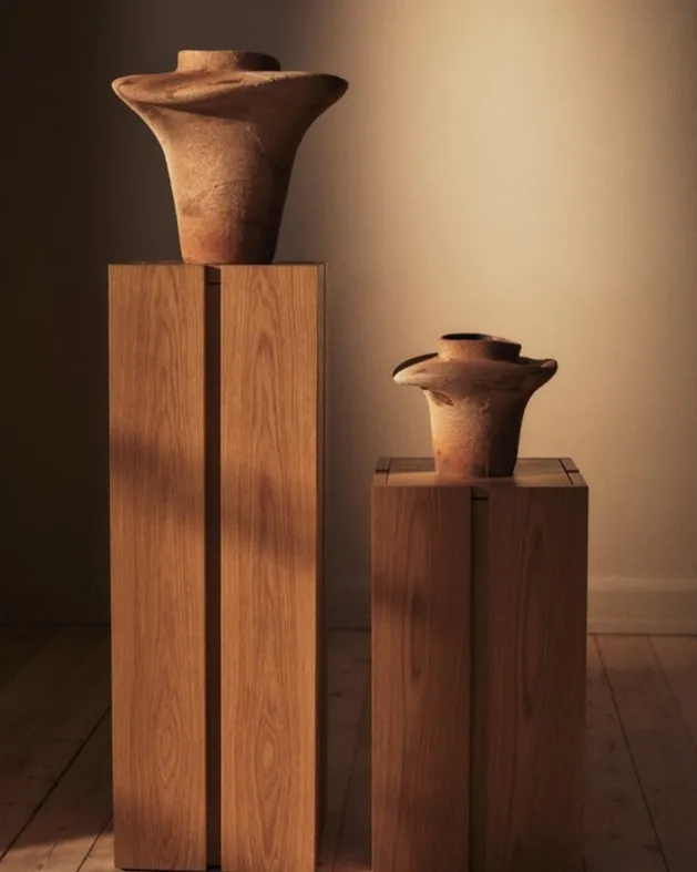 Deux vases en céramique évasés, couleur terre, sur des socles en bois clair.