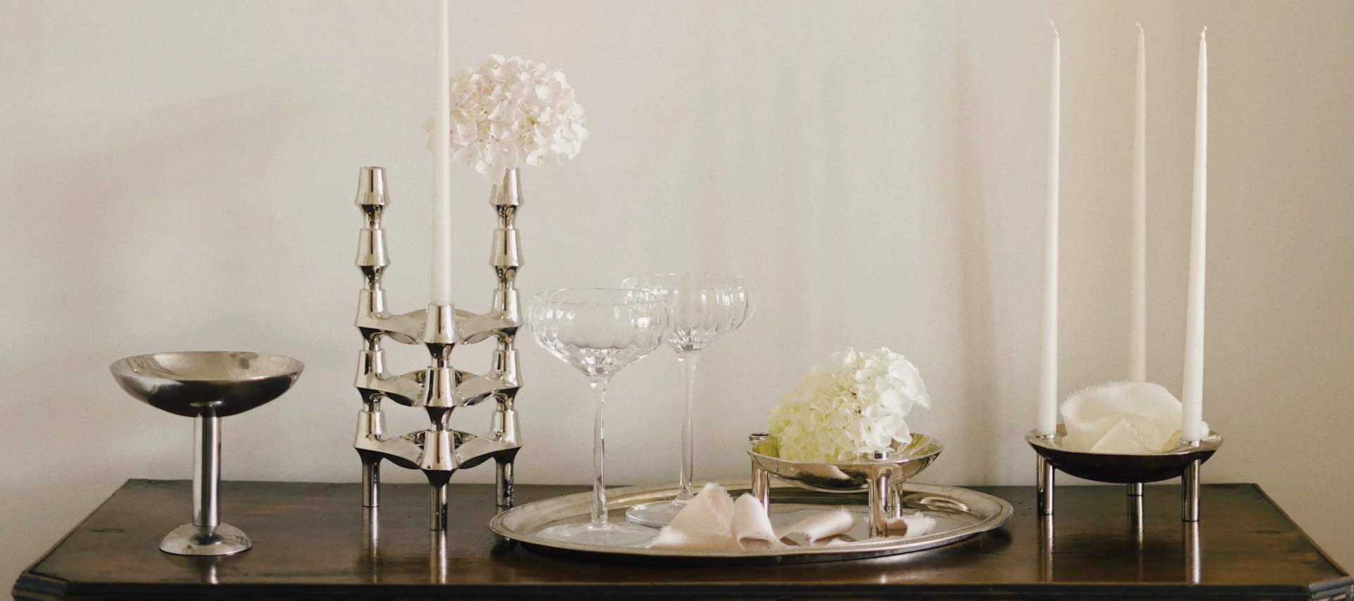 Élégante décoration avec chandeliers argentés, bougies, coupes en verre et hortensias blancs sur bois.